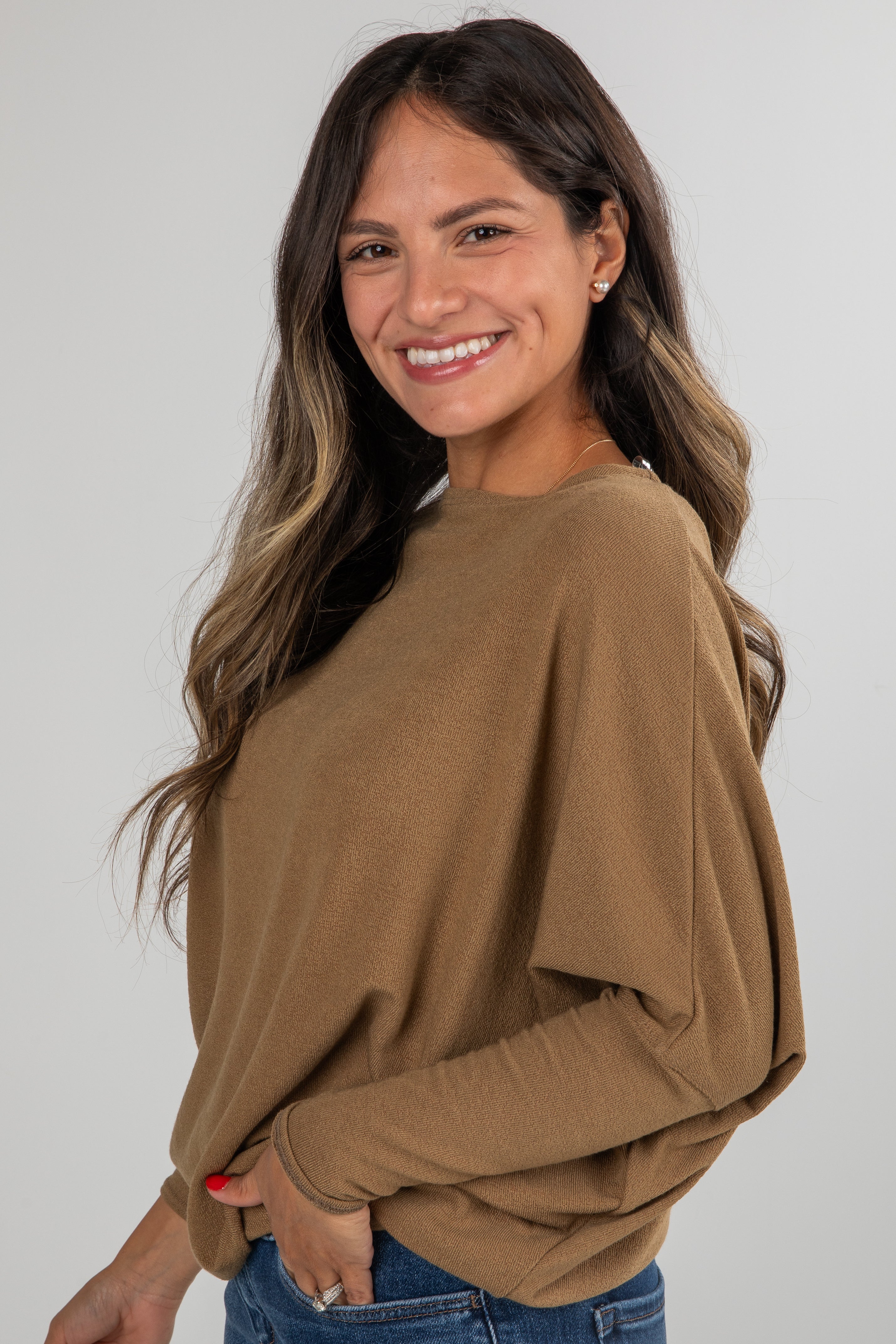 Woman wearing a brown sweater and blue jeans against a white background