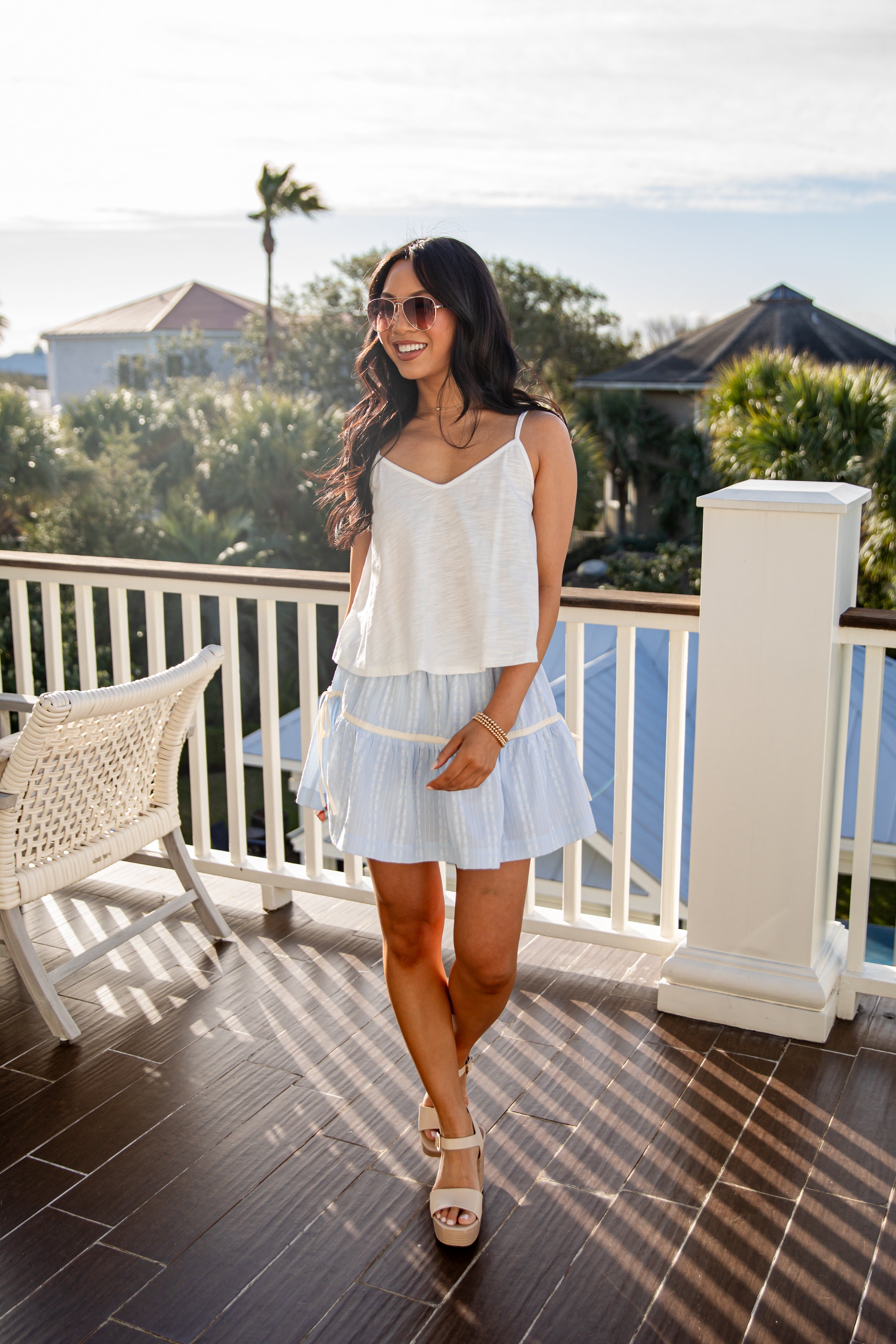Woman in a white top and light blue skirt standing on a balcony with a scenic view.