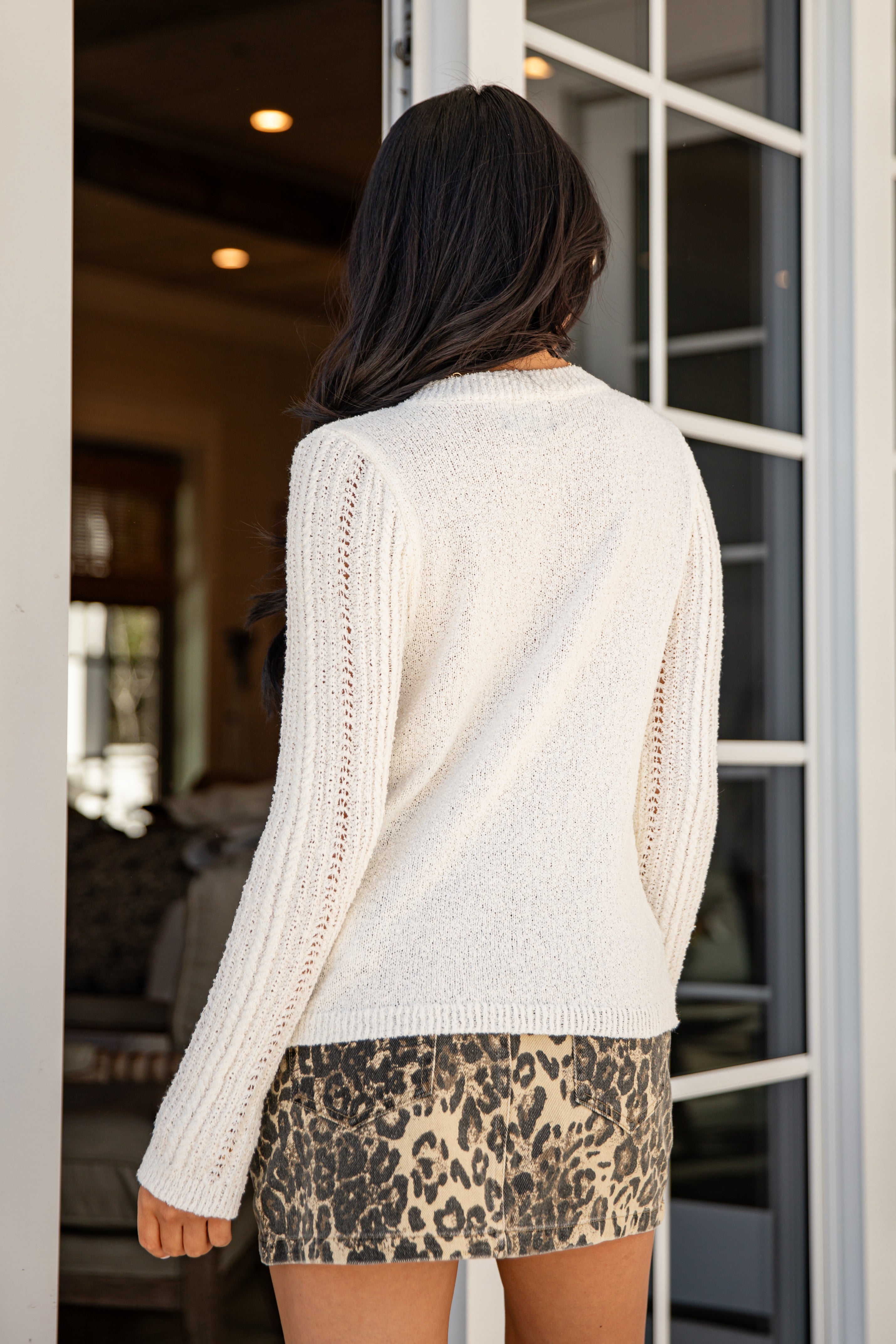Woman wearing a white sweater and leopard print shorts standing in a doorway.