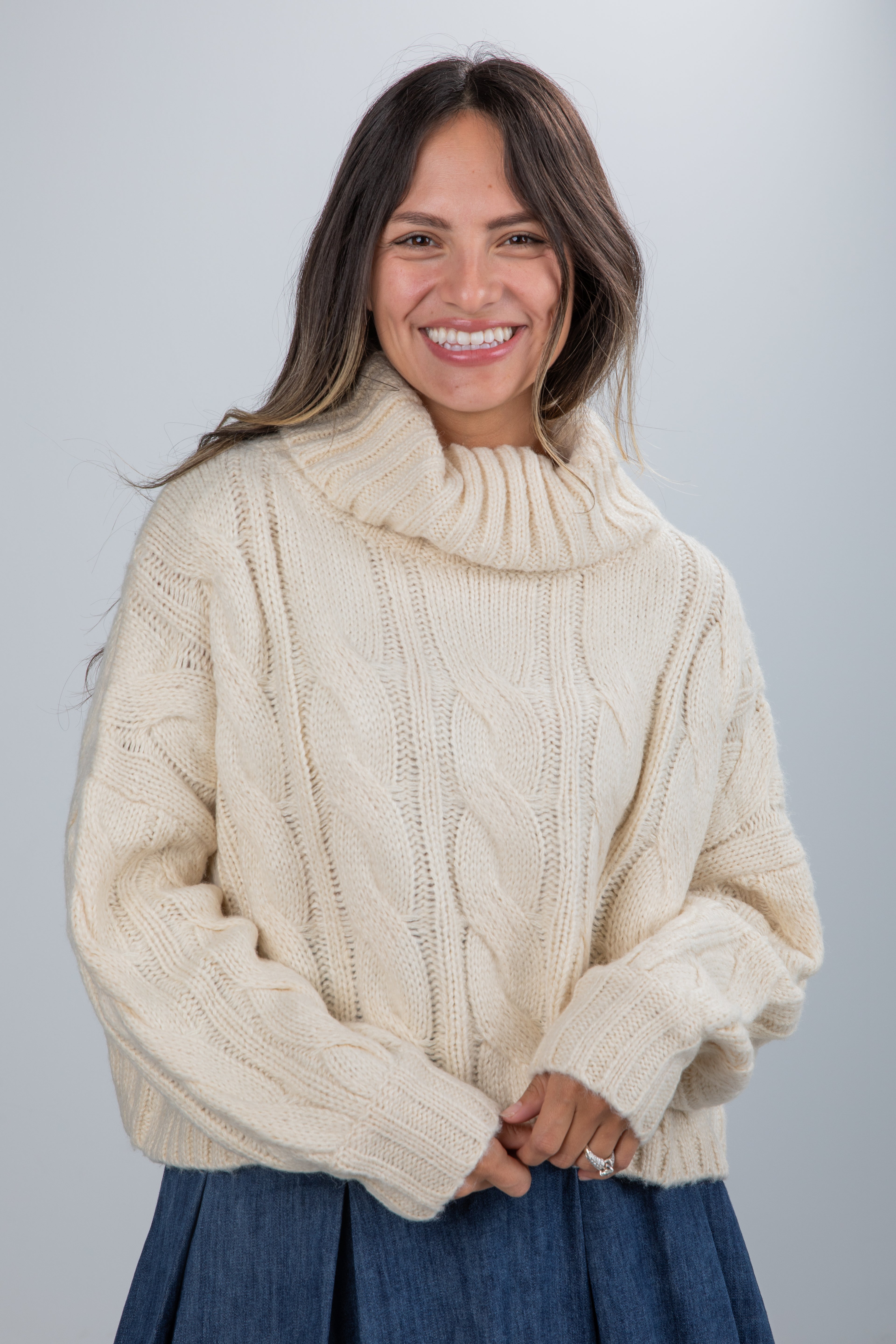 Woman wearing a cream cable knit sweater against a plain background