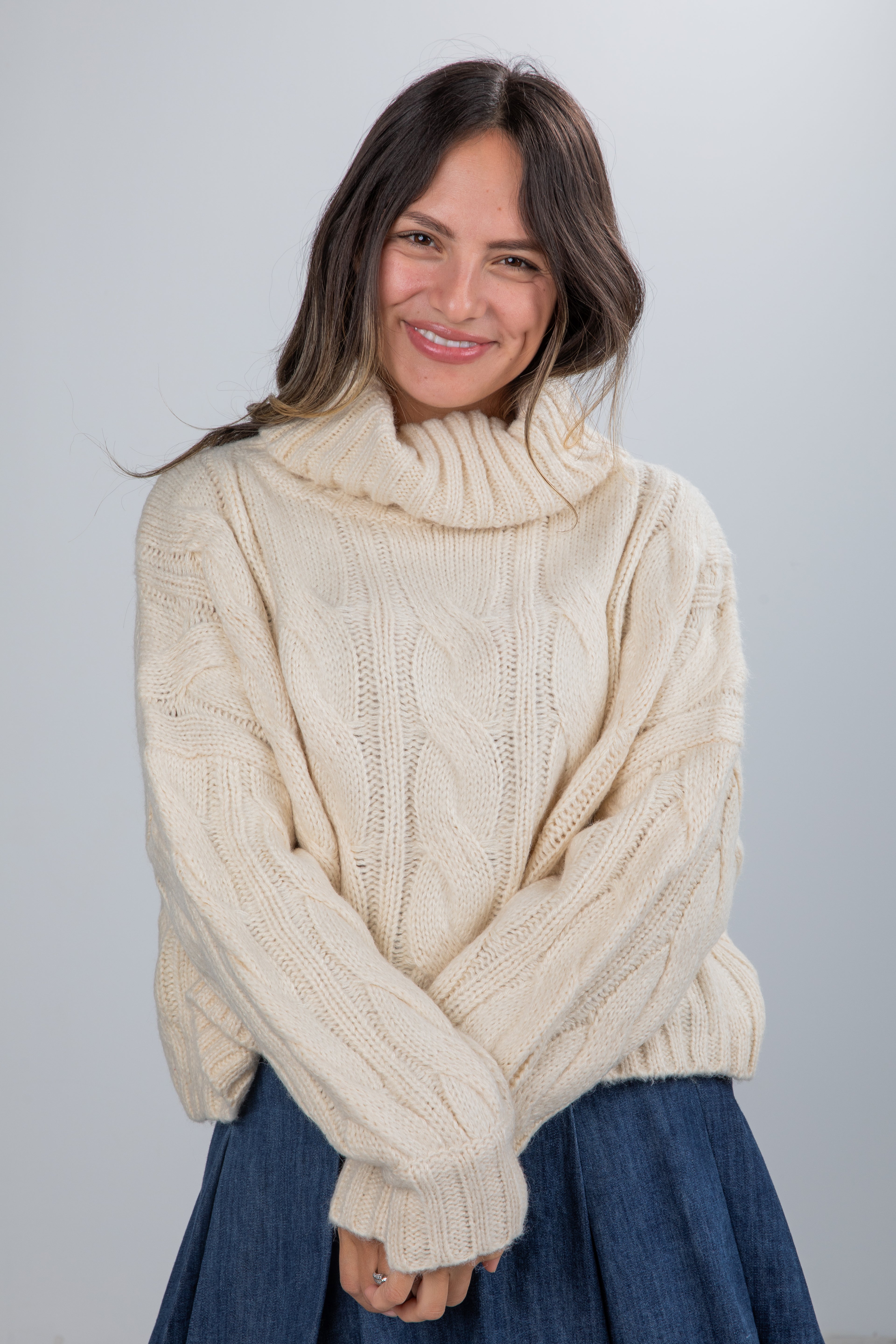 Woman wearing a cream cable knit sweater against a plain background