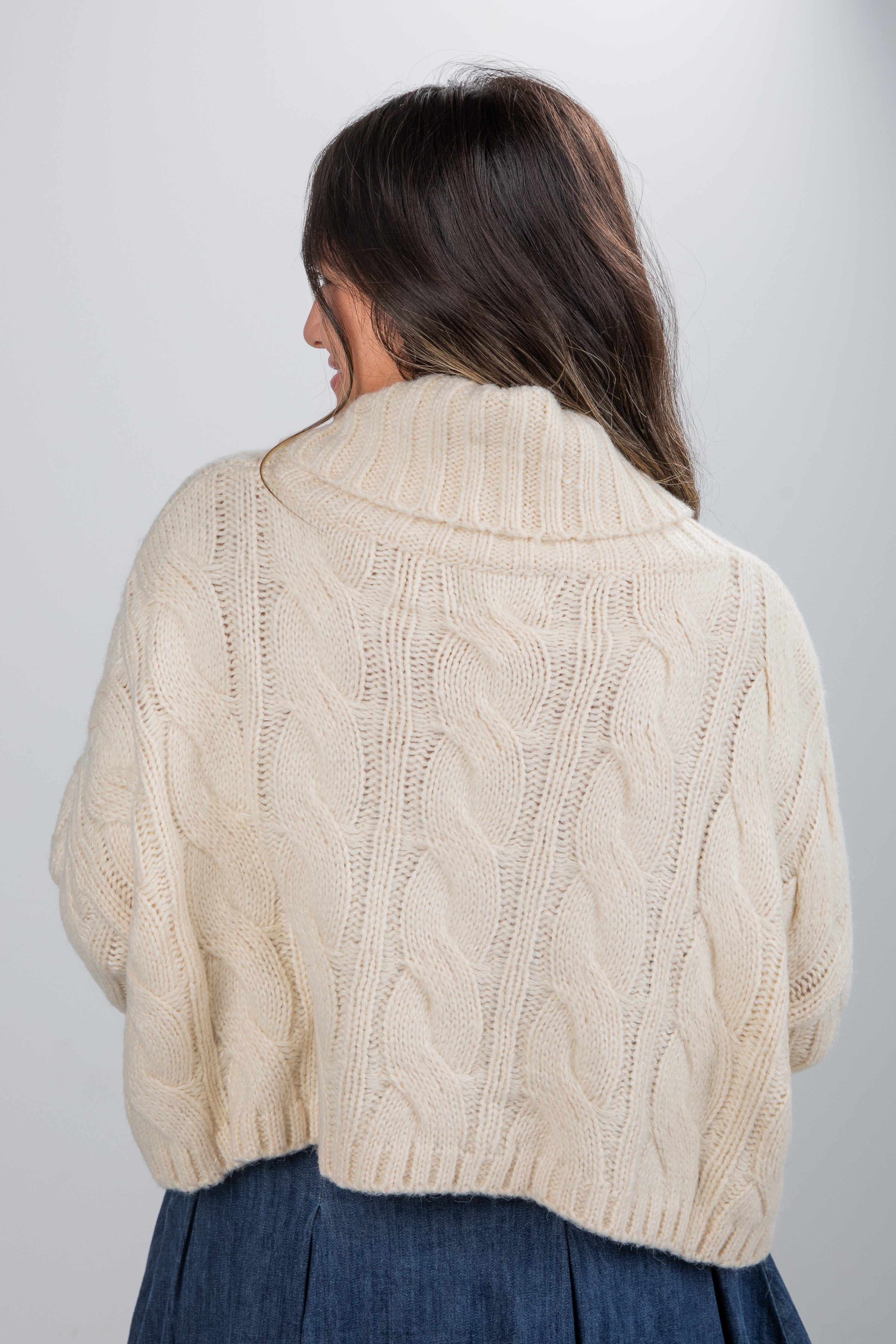 Woman wearing a beige cable knit sweater against a plain background