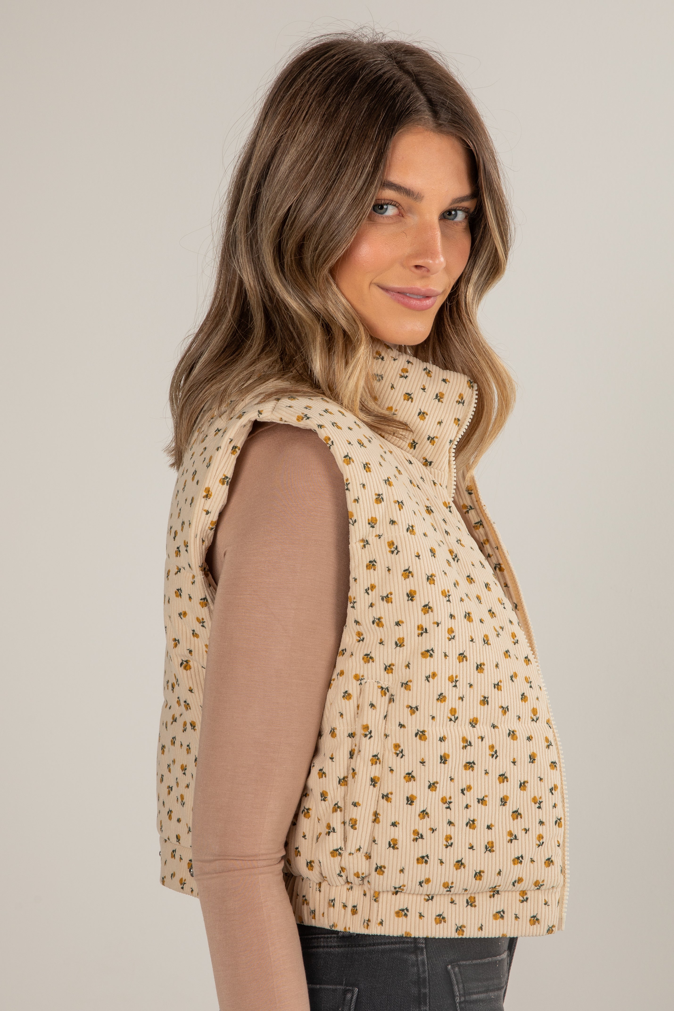 Woman wearing a beige patterned vest over a brown shirt on a plain background