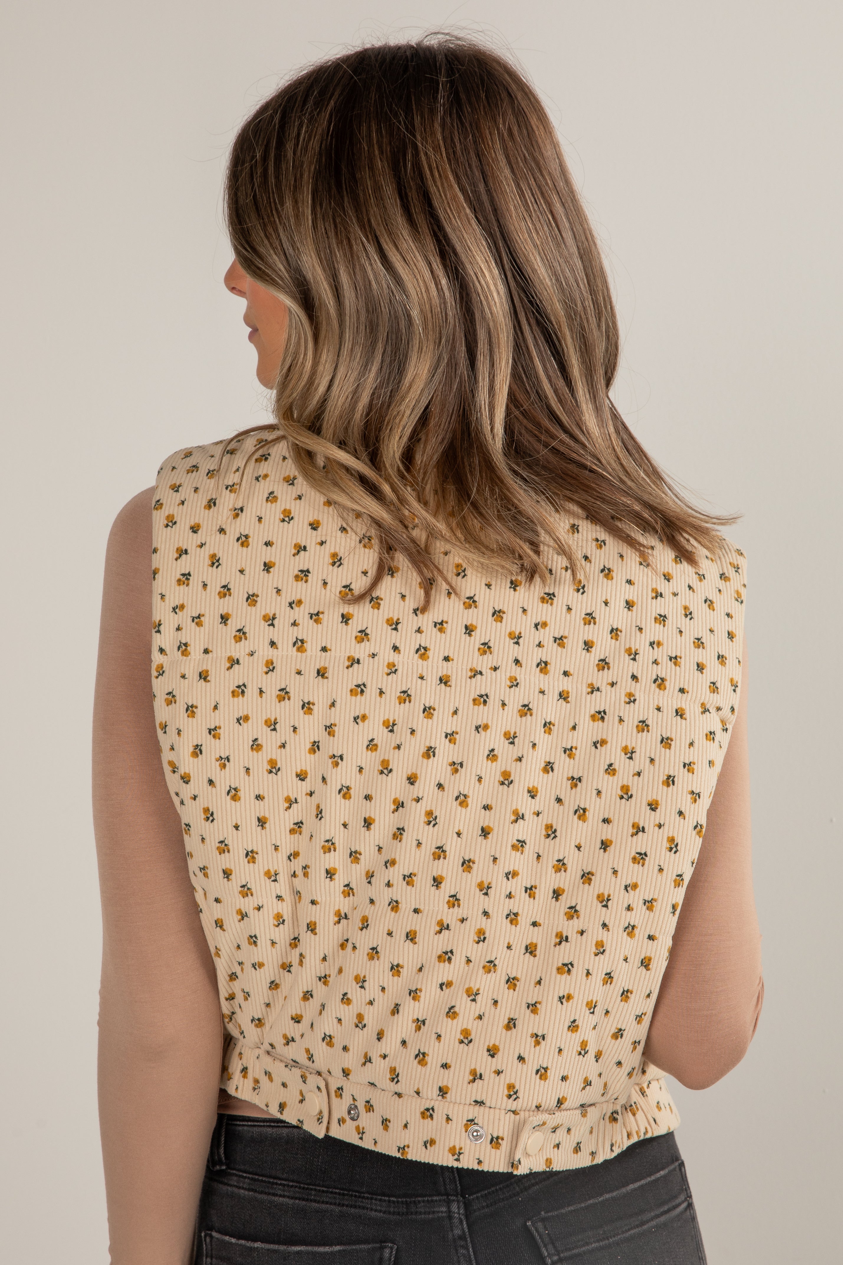 Woman wearing a beige sleeveless top with a subtle pattern on a plain background