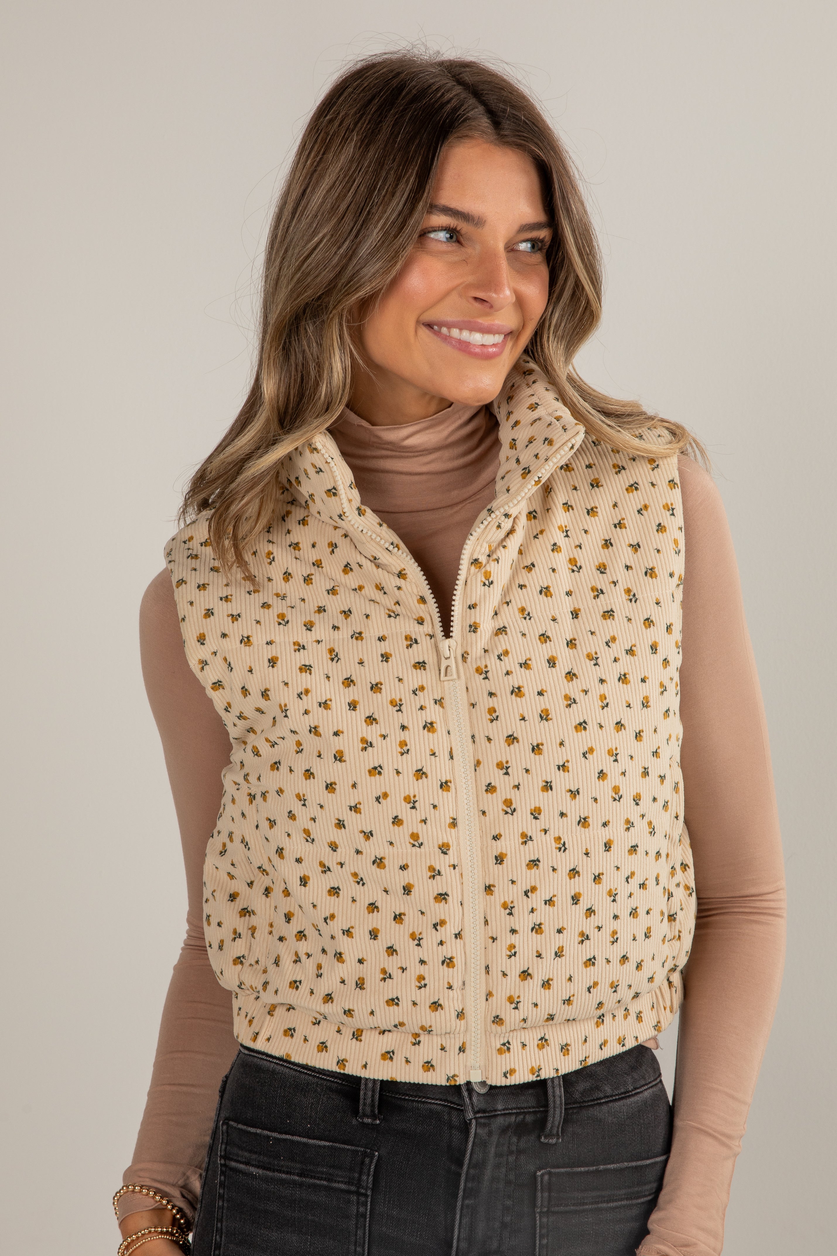 Woman wearing a beige patterned vest over a brown long-sleeve shirt against a neutral background