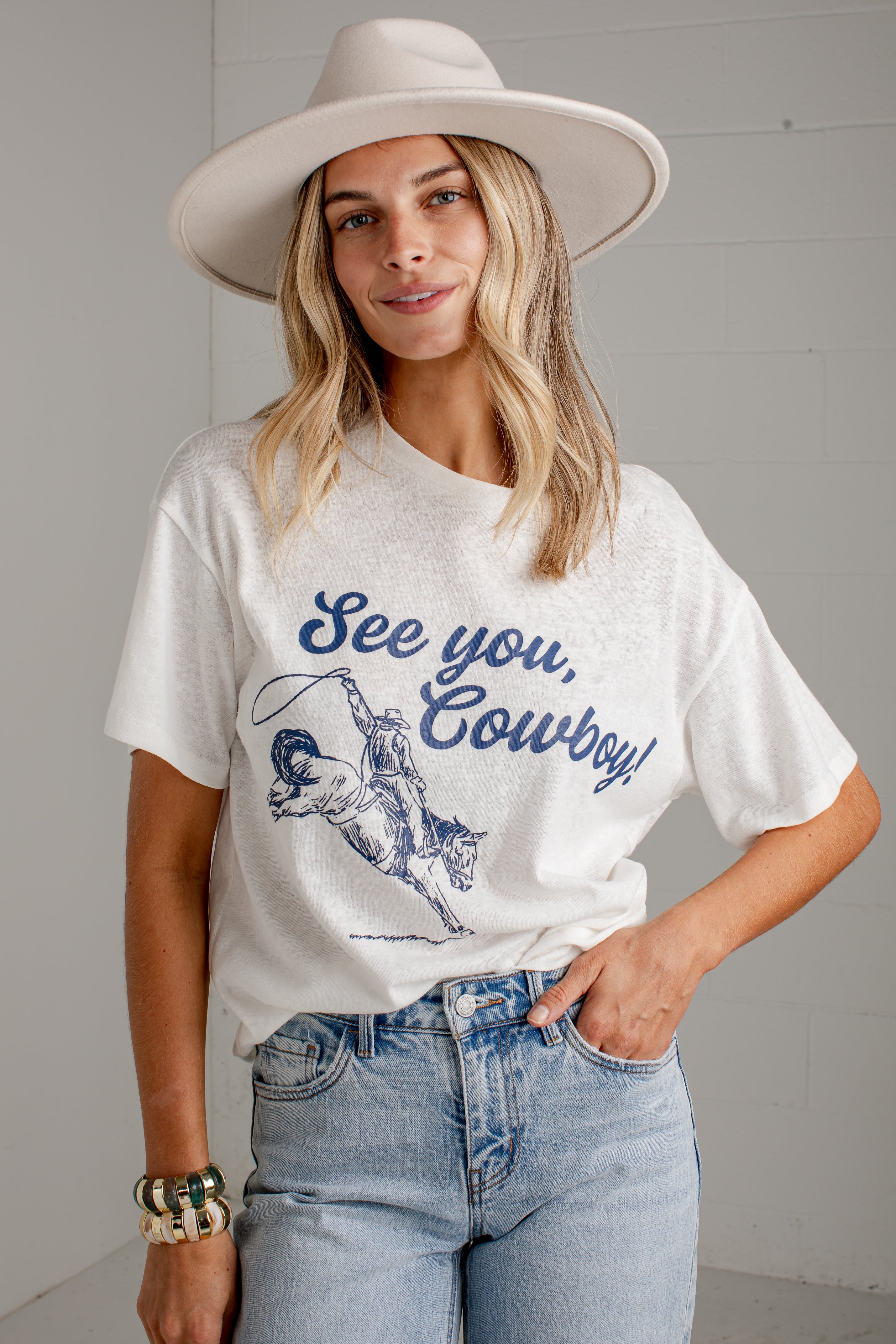 A woman wearing a white graphic t-shirt with a blue cowboy design and the text &