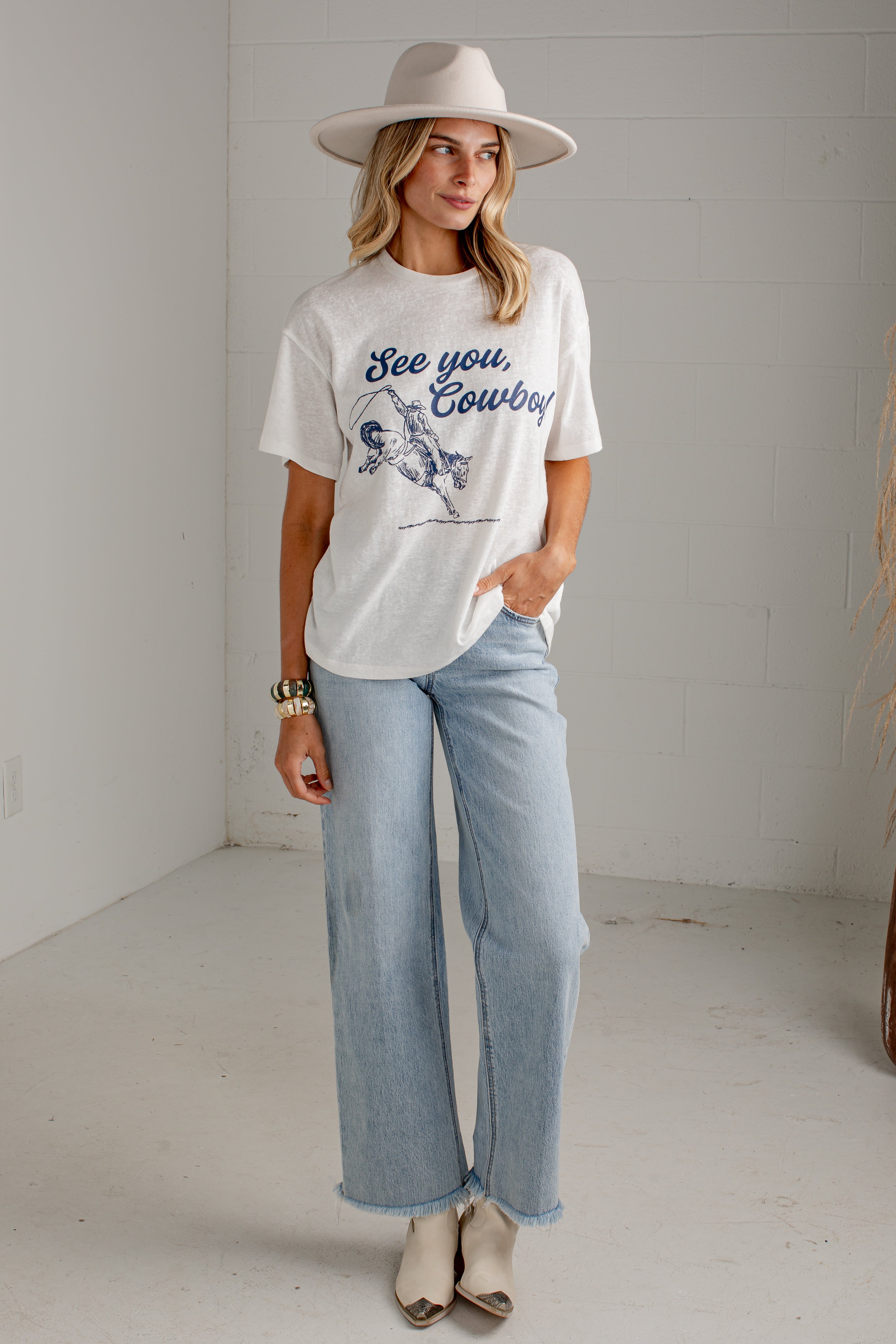 A woman wearing a white graphic t-shirt with a blue cowboy design and the text &