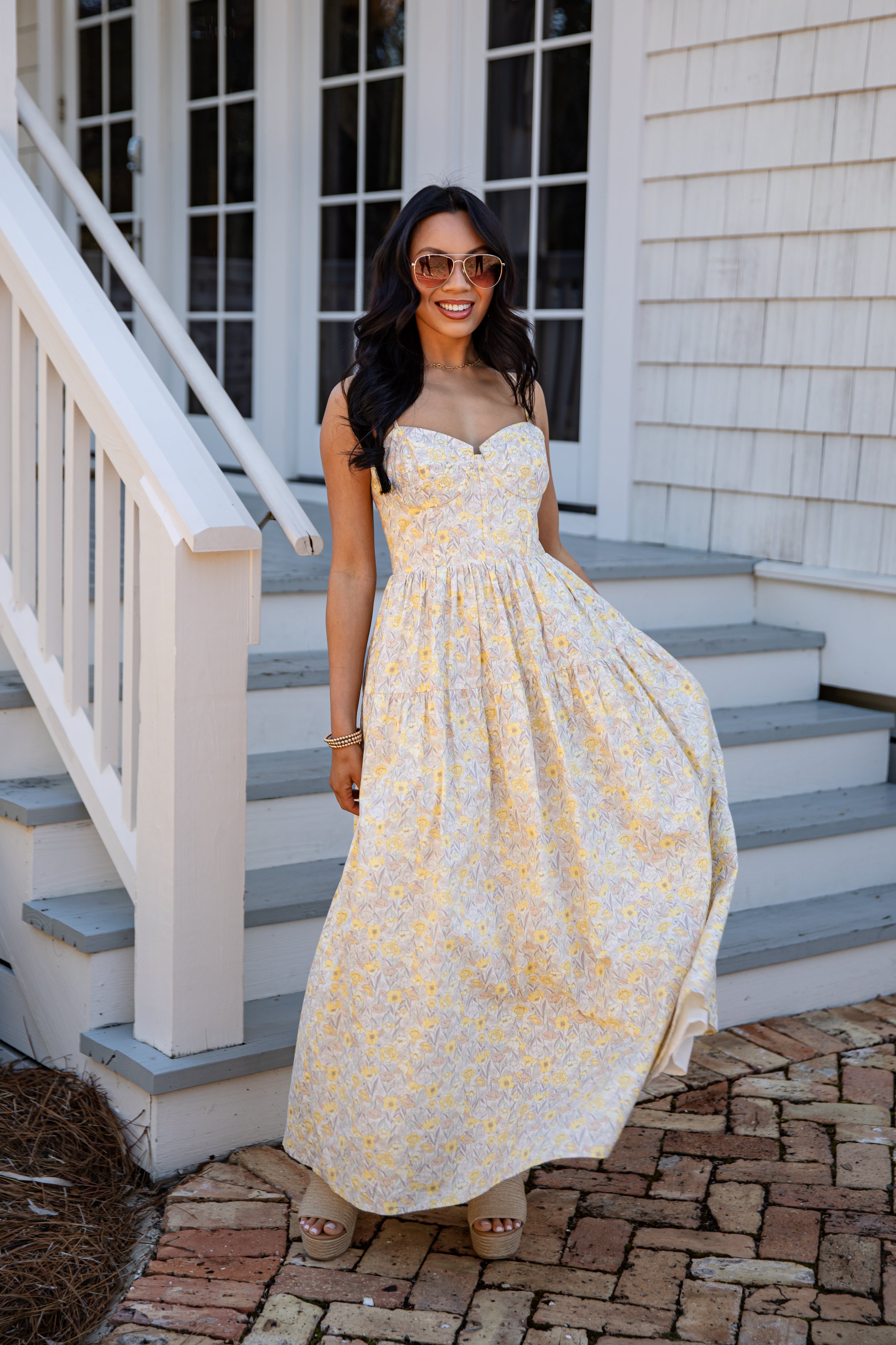 Woman in a yellow floral dress standing on a staircase outside a house.