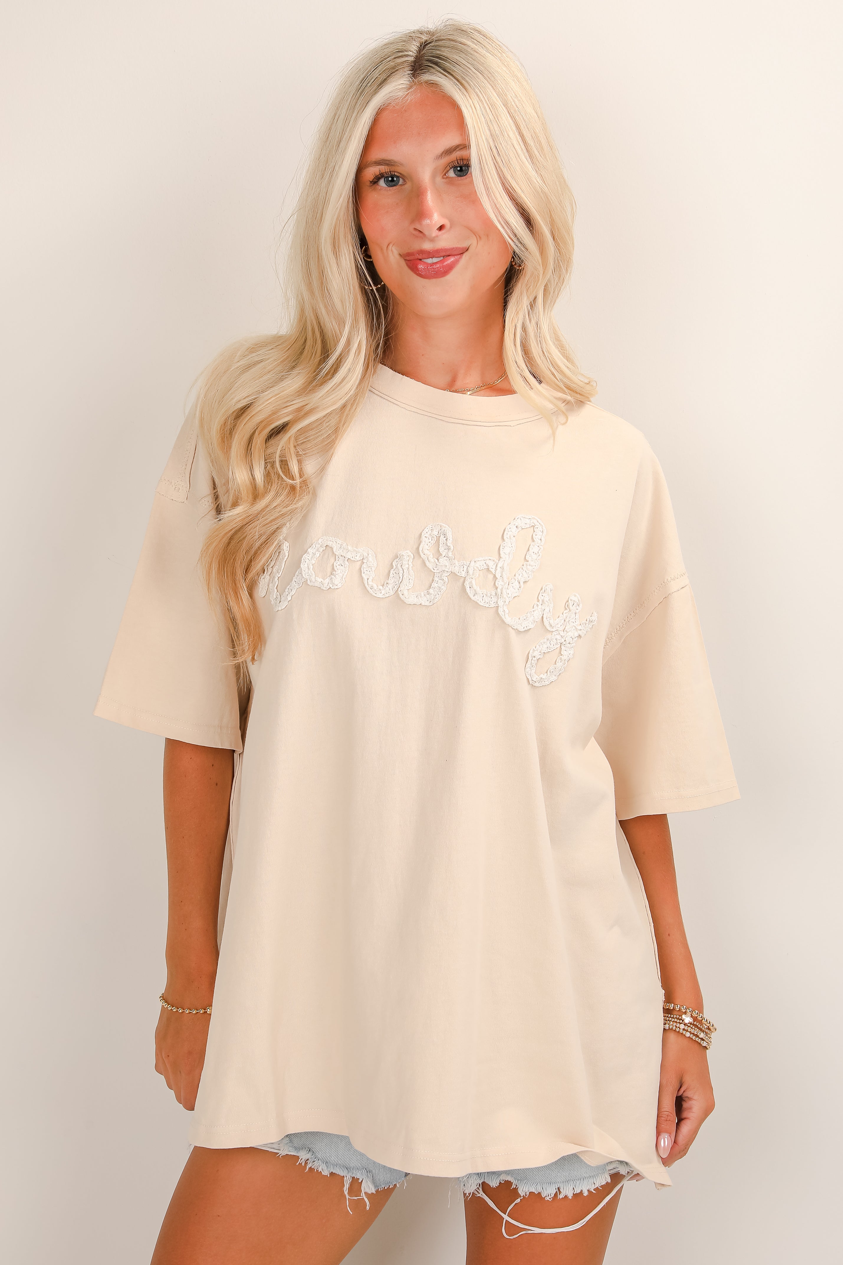 Woman wearing a beige oversized t-shirt with text on a plain background