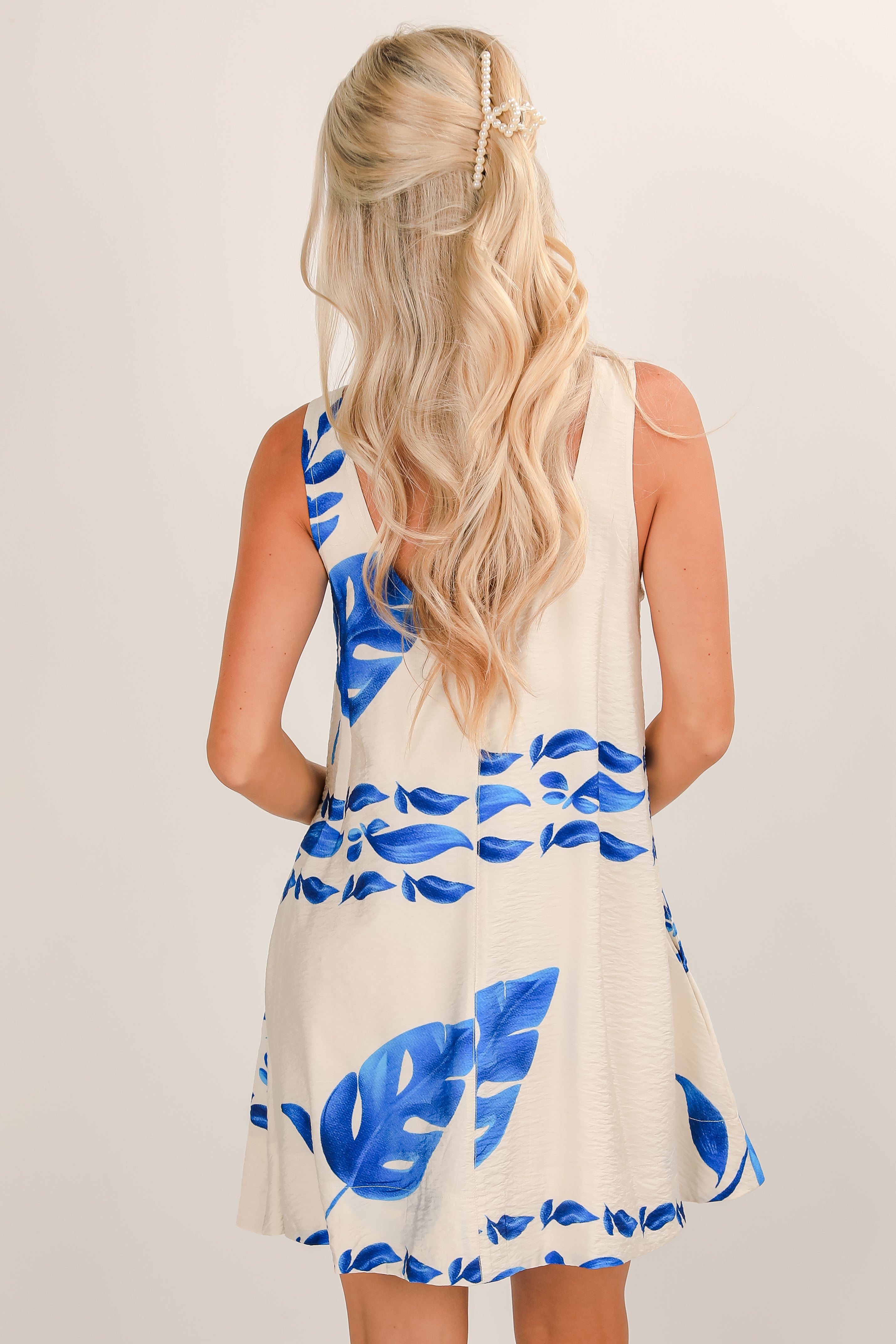 Woman wearing a white dress with blue leaf patterns on a plain background