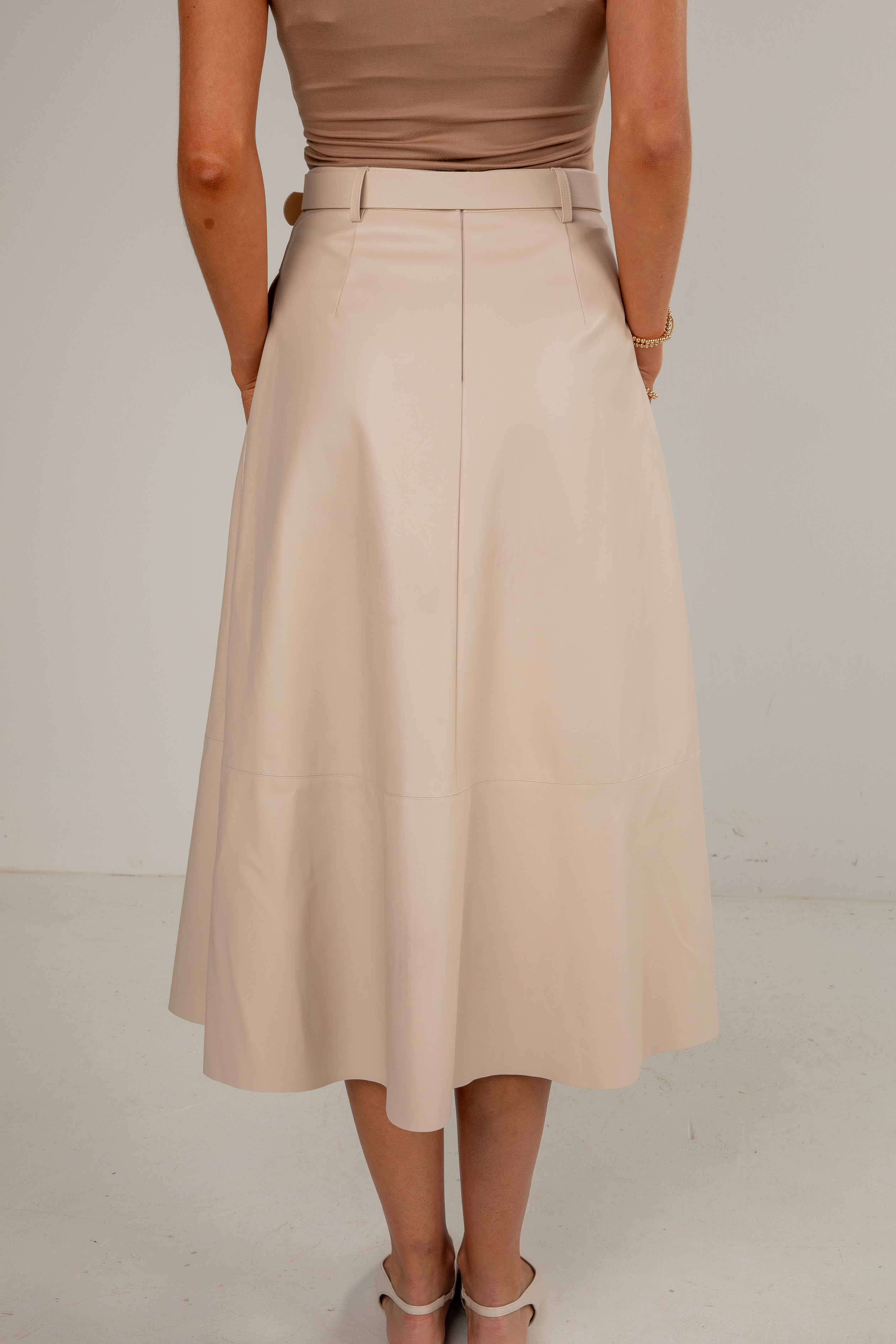 Person wearing a beige skirt and brown top on a plain background