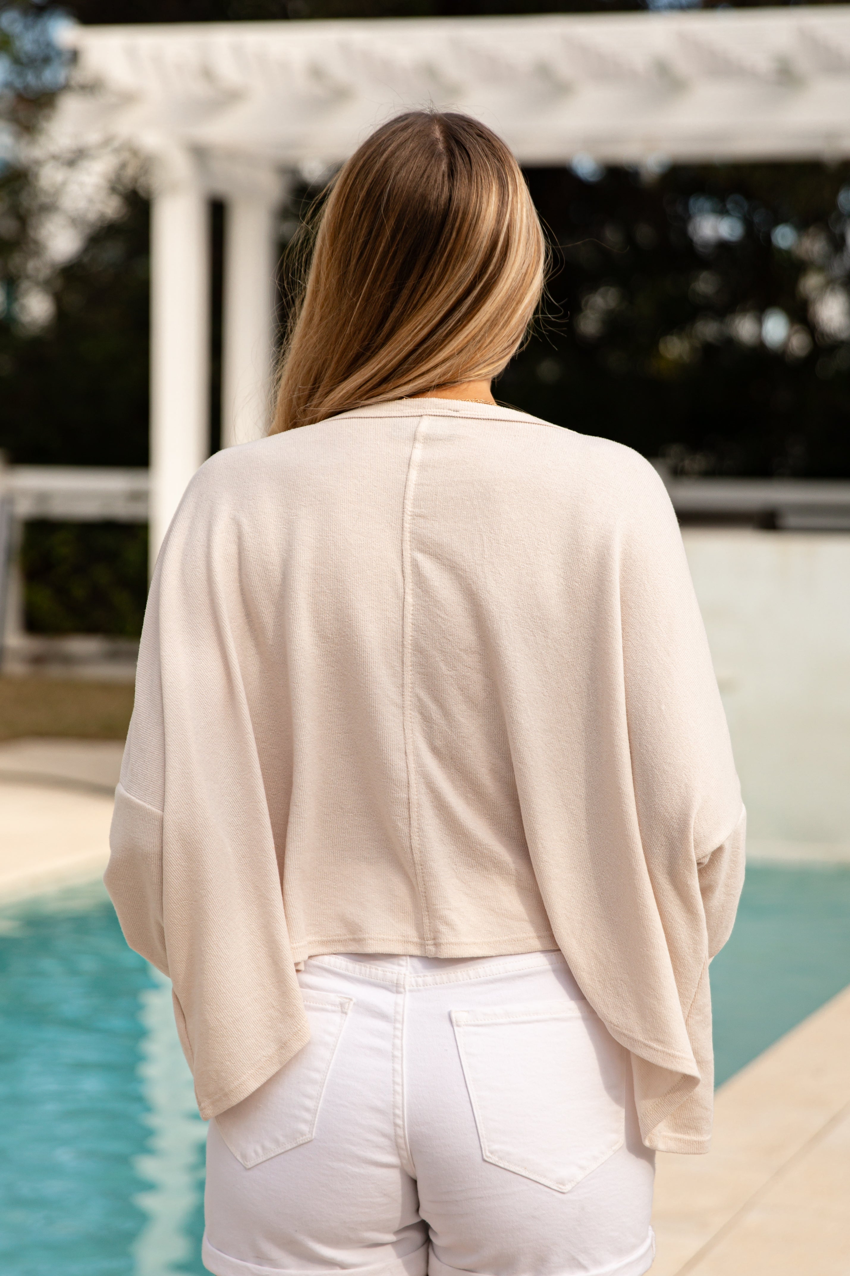 Woman wearing a beige cardigan and white pants by a pool
