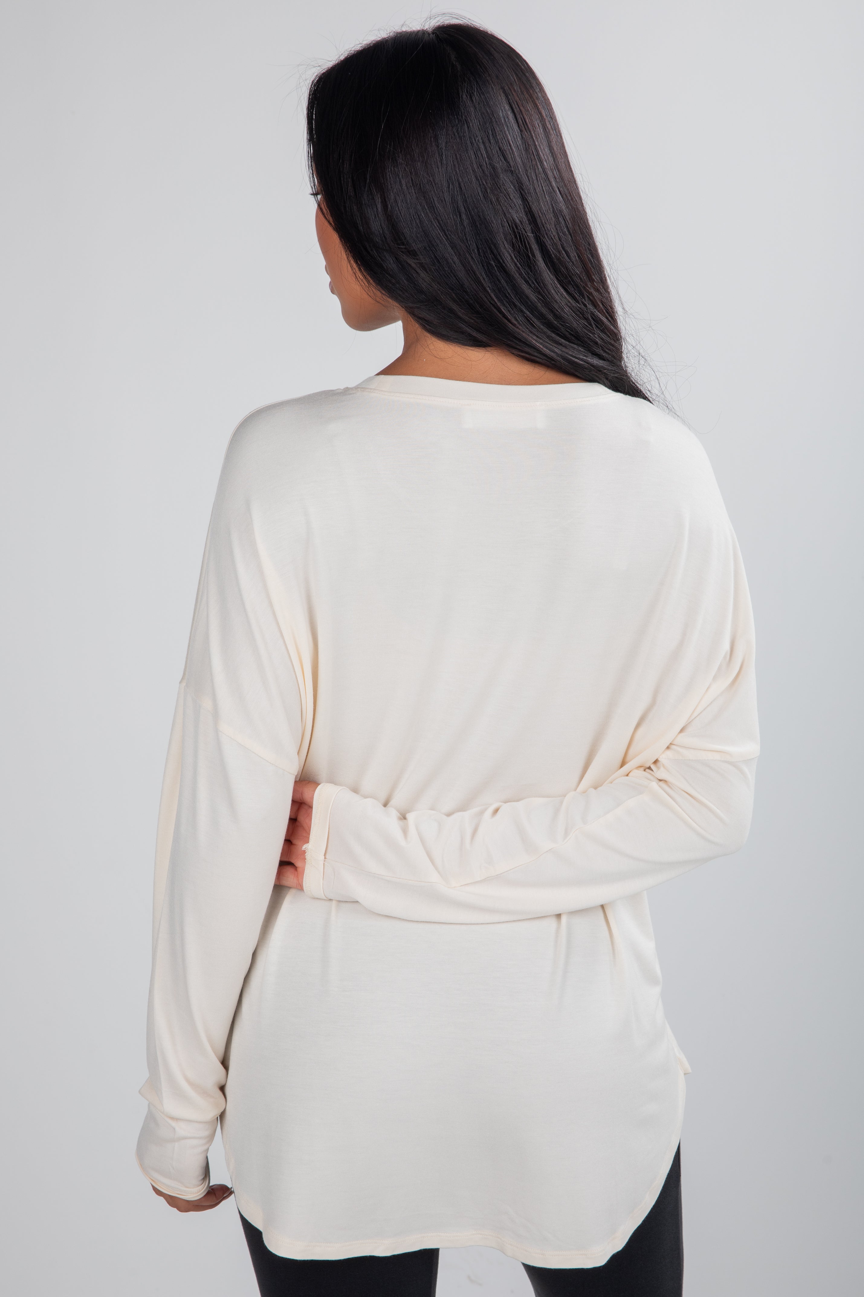 Woman wearing a cream-colored long-sleeve top with a knot detail on a white background