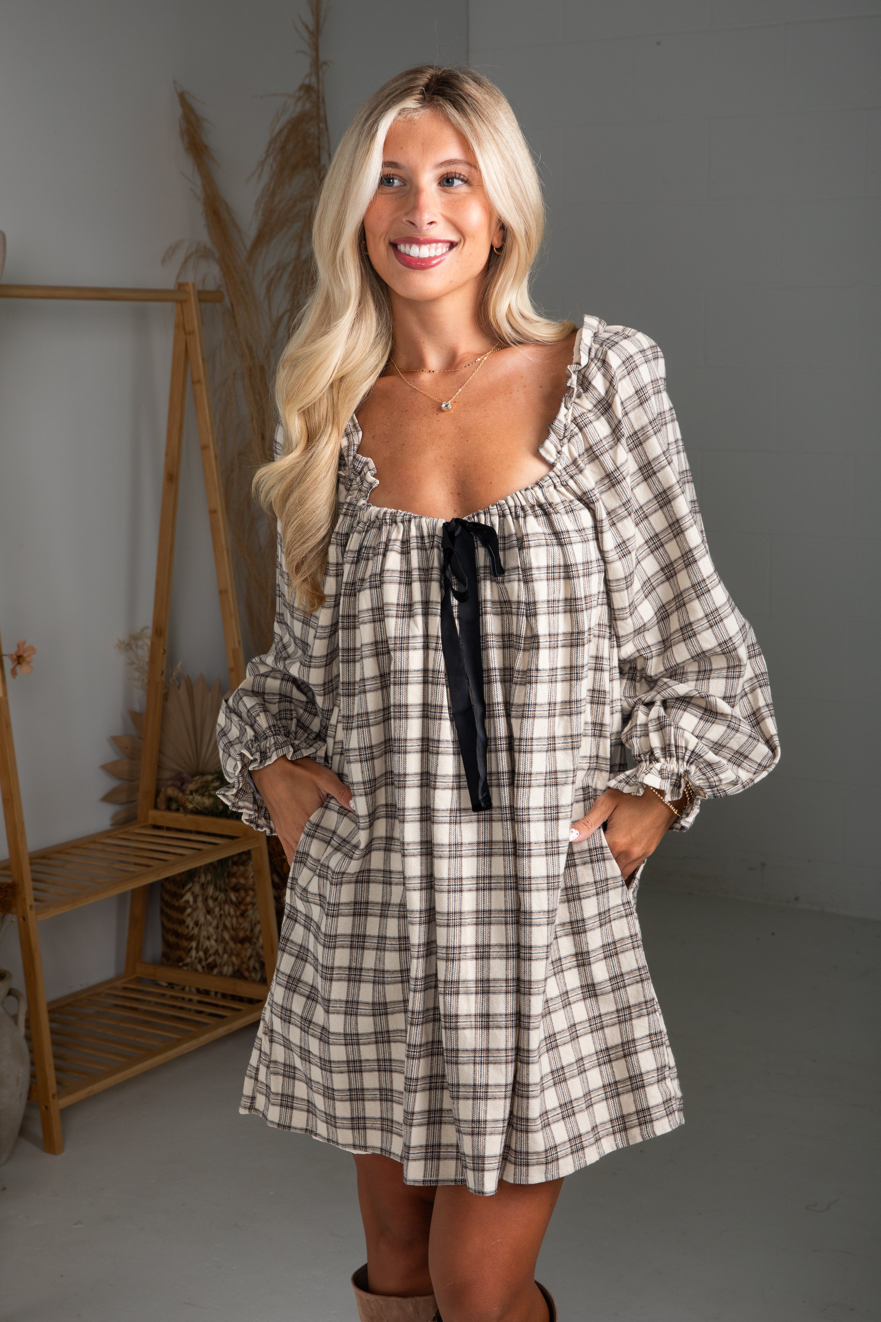 Woman wearing a plaid dress with a black ribbon in a minimalistic room.