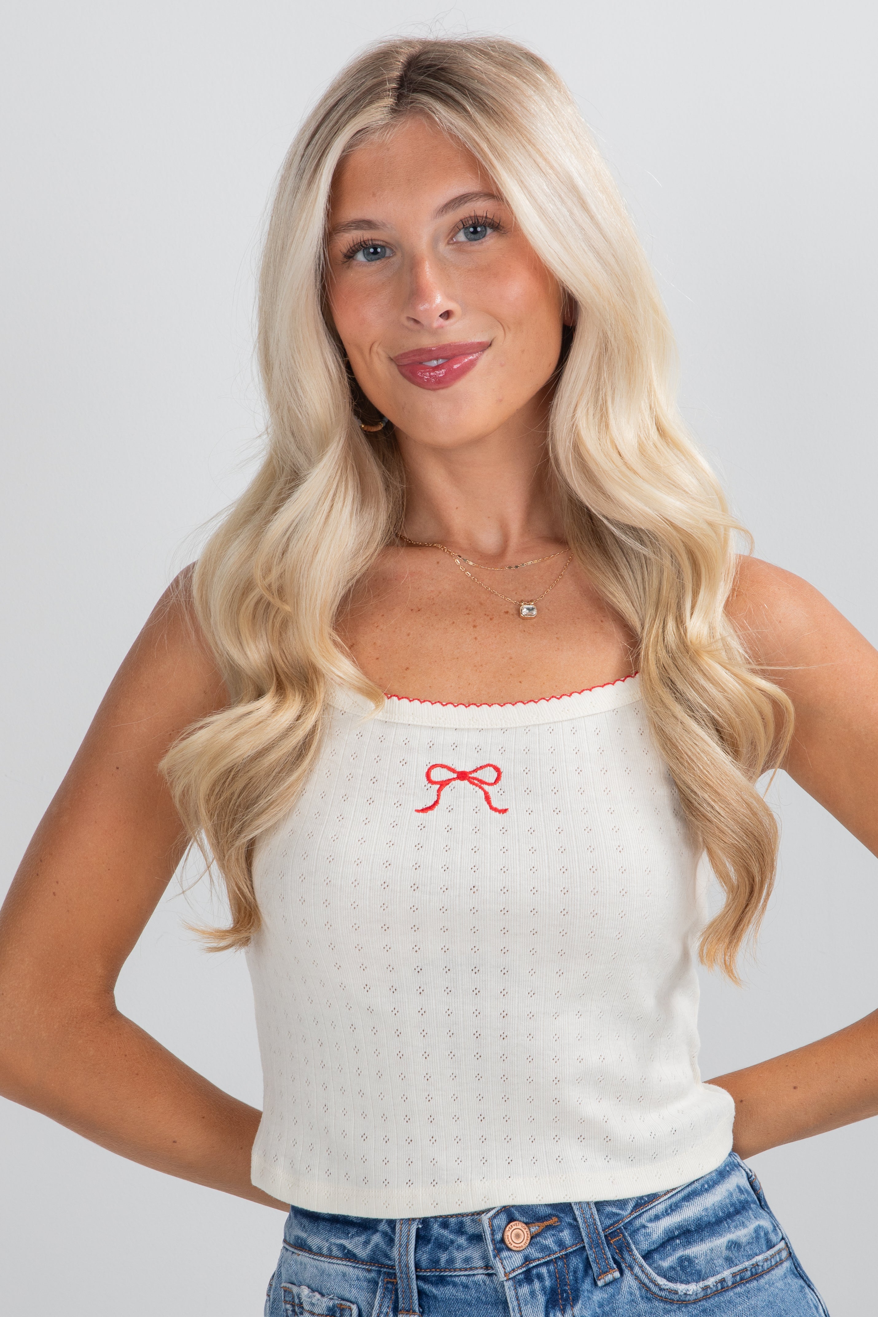 Woman wearing a white tank top with a red bow design on a plain background