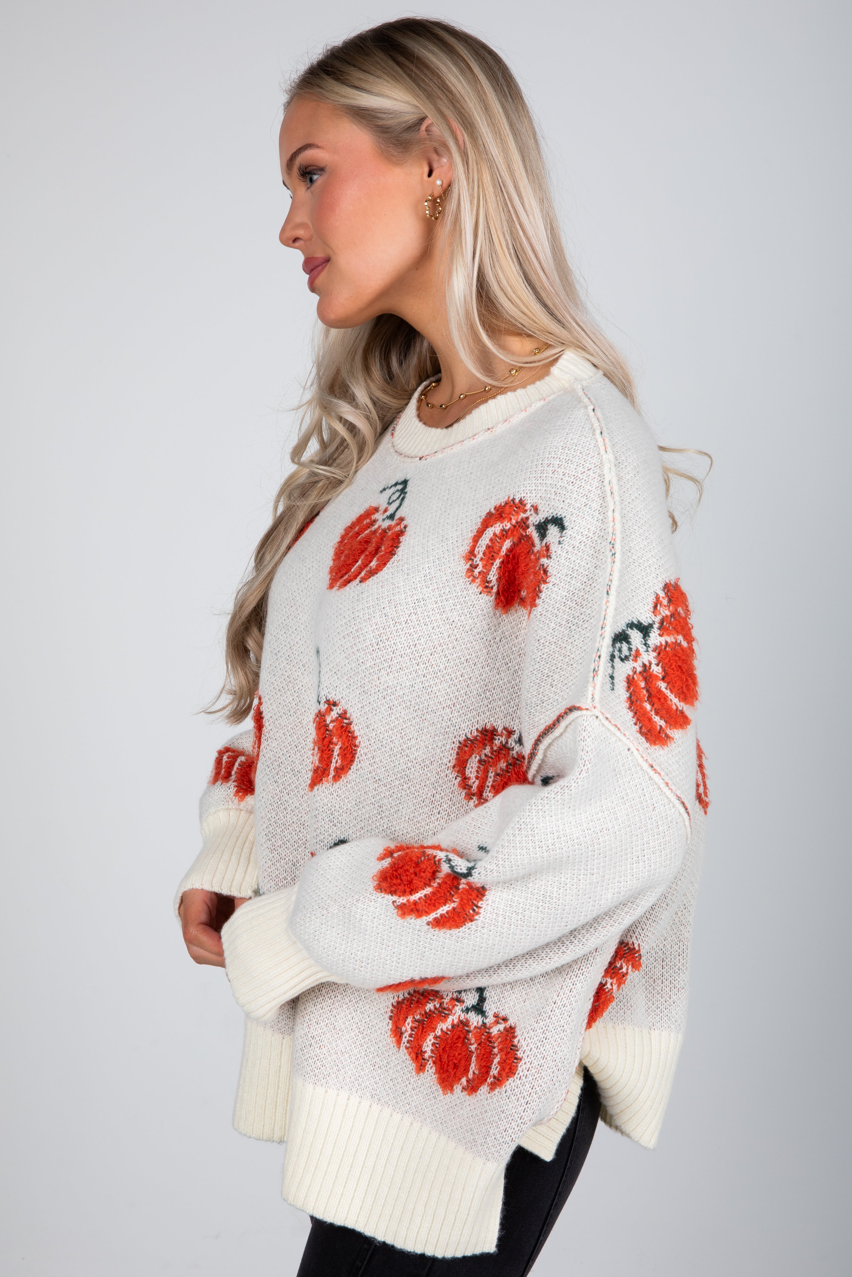 Woman wearing a white sweater with red floral patterns on a plain background