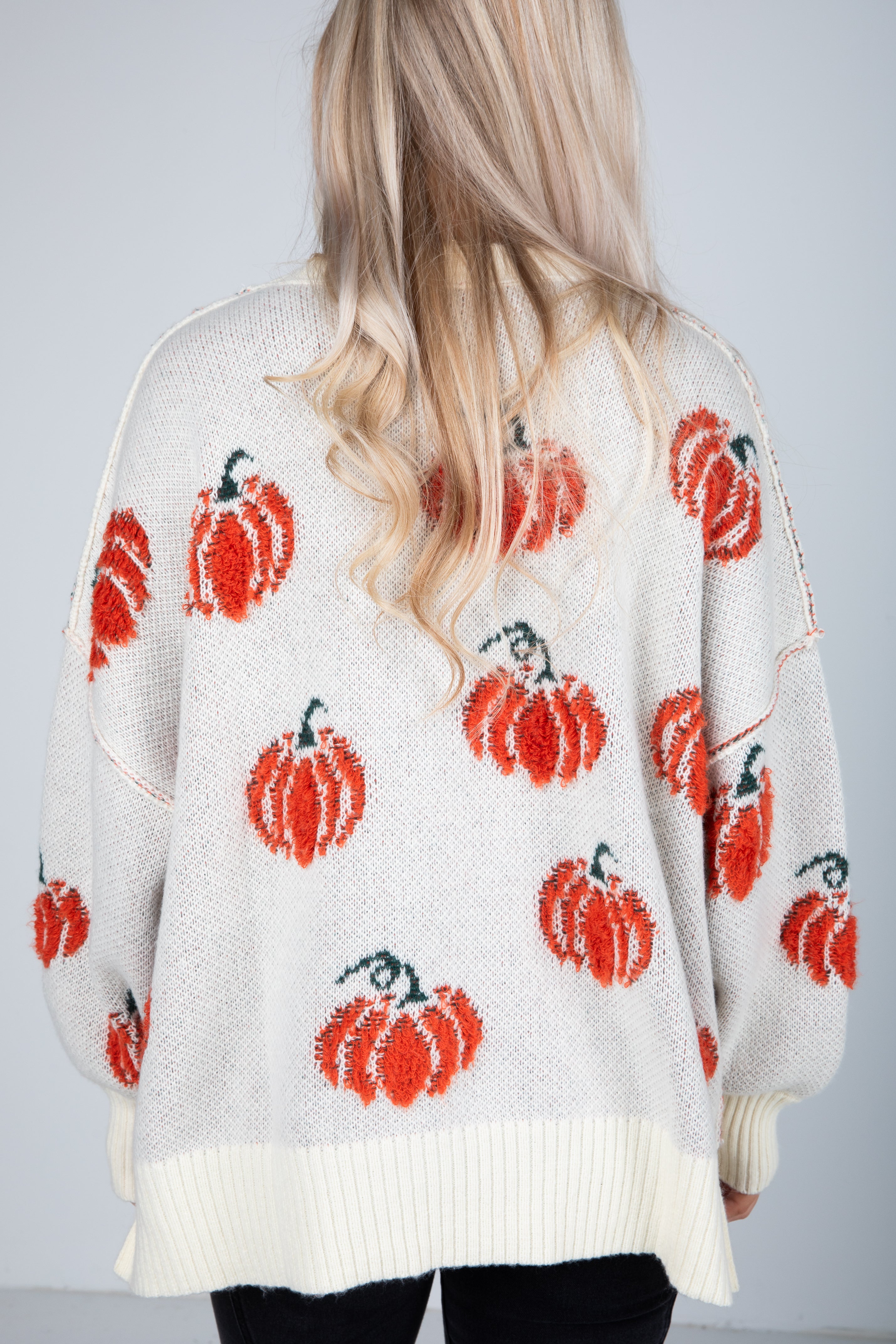 White sweater with red pumpkin patterns worn by a person with blonde hair.