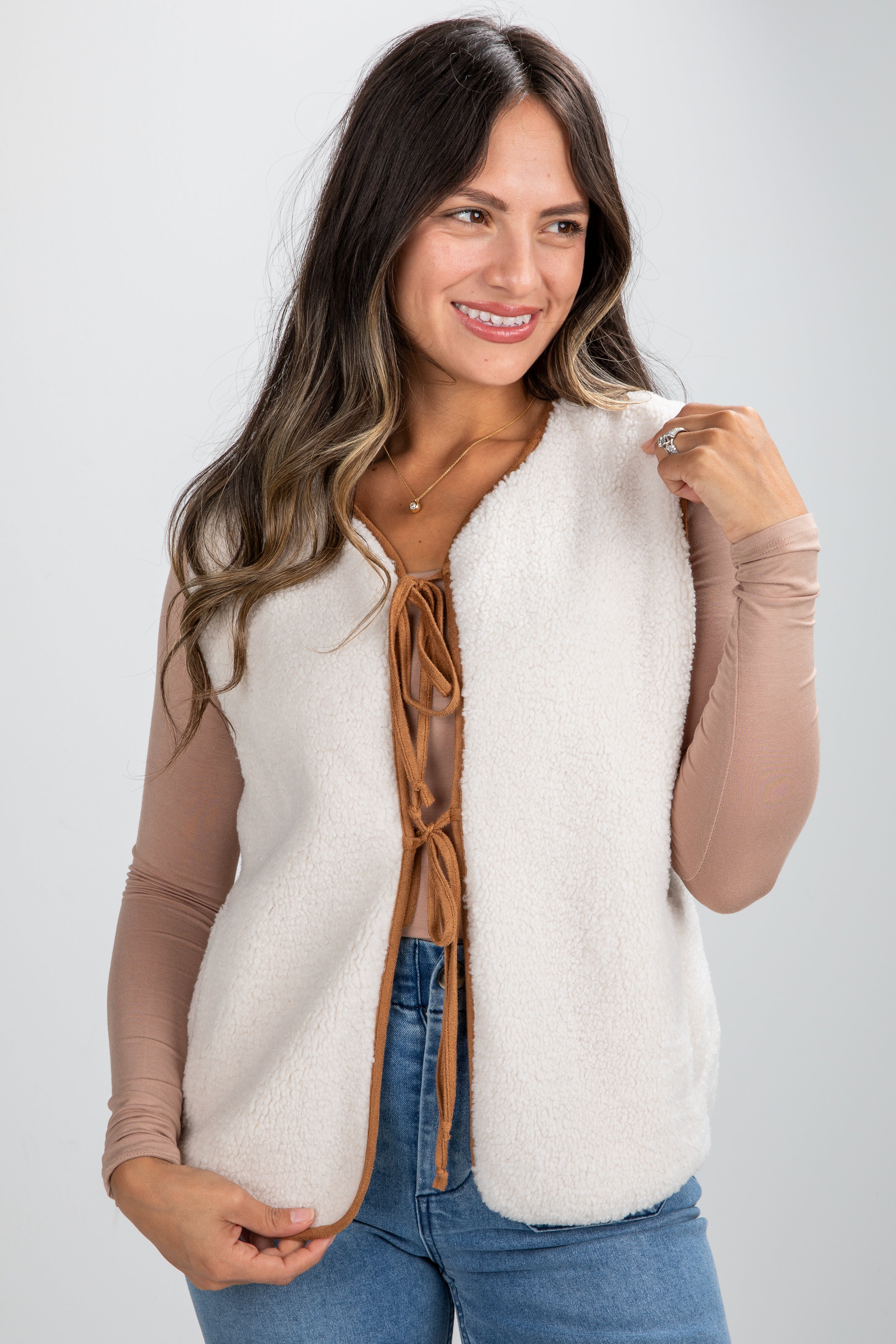 Woman wearing a white fleece vest with brown accents on a plain background