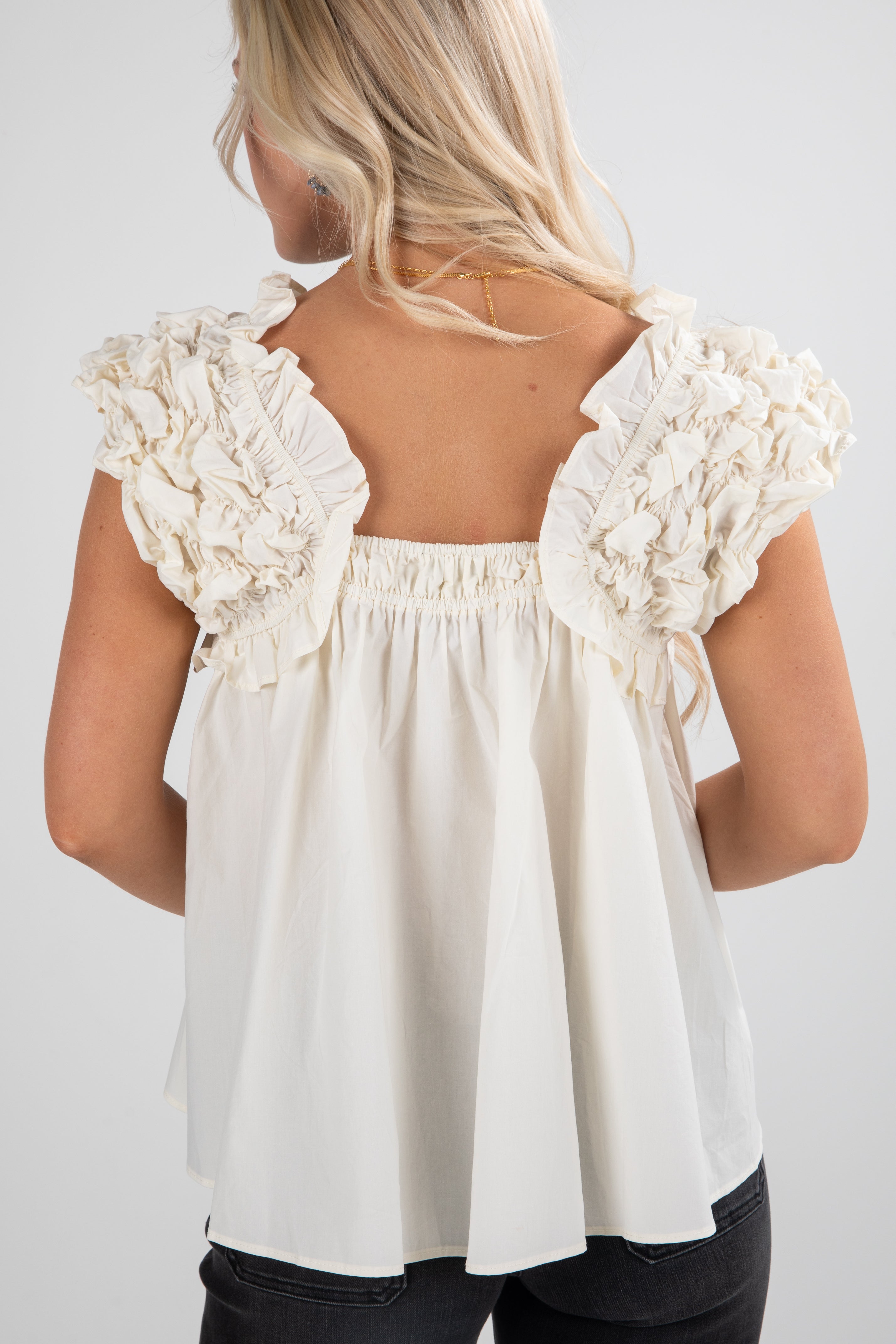 White blouse with ruffled shoulders on a plain background