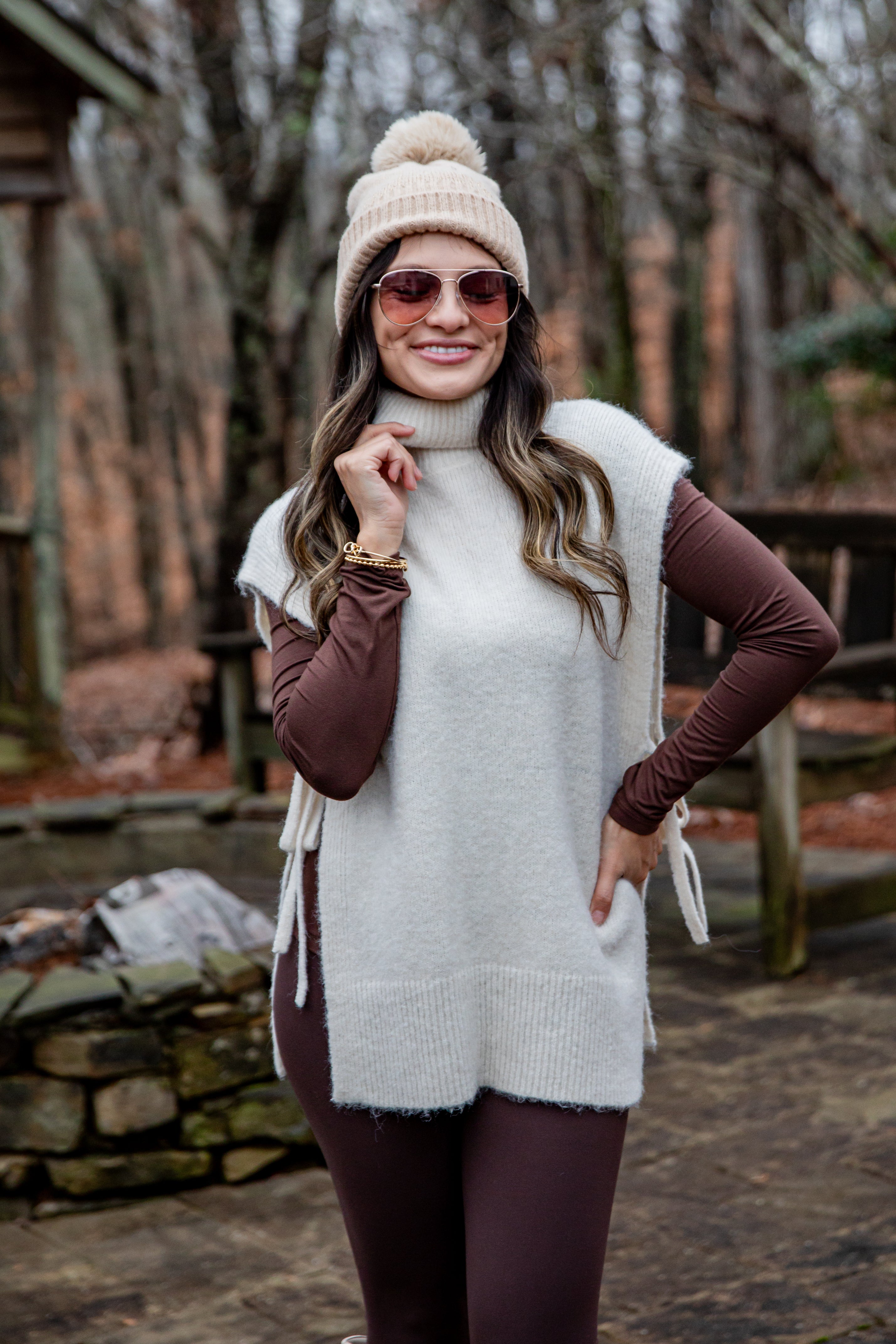 Woman wearing a white vest, brown long-sleeve top, and beige beanie outdoors.