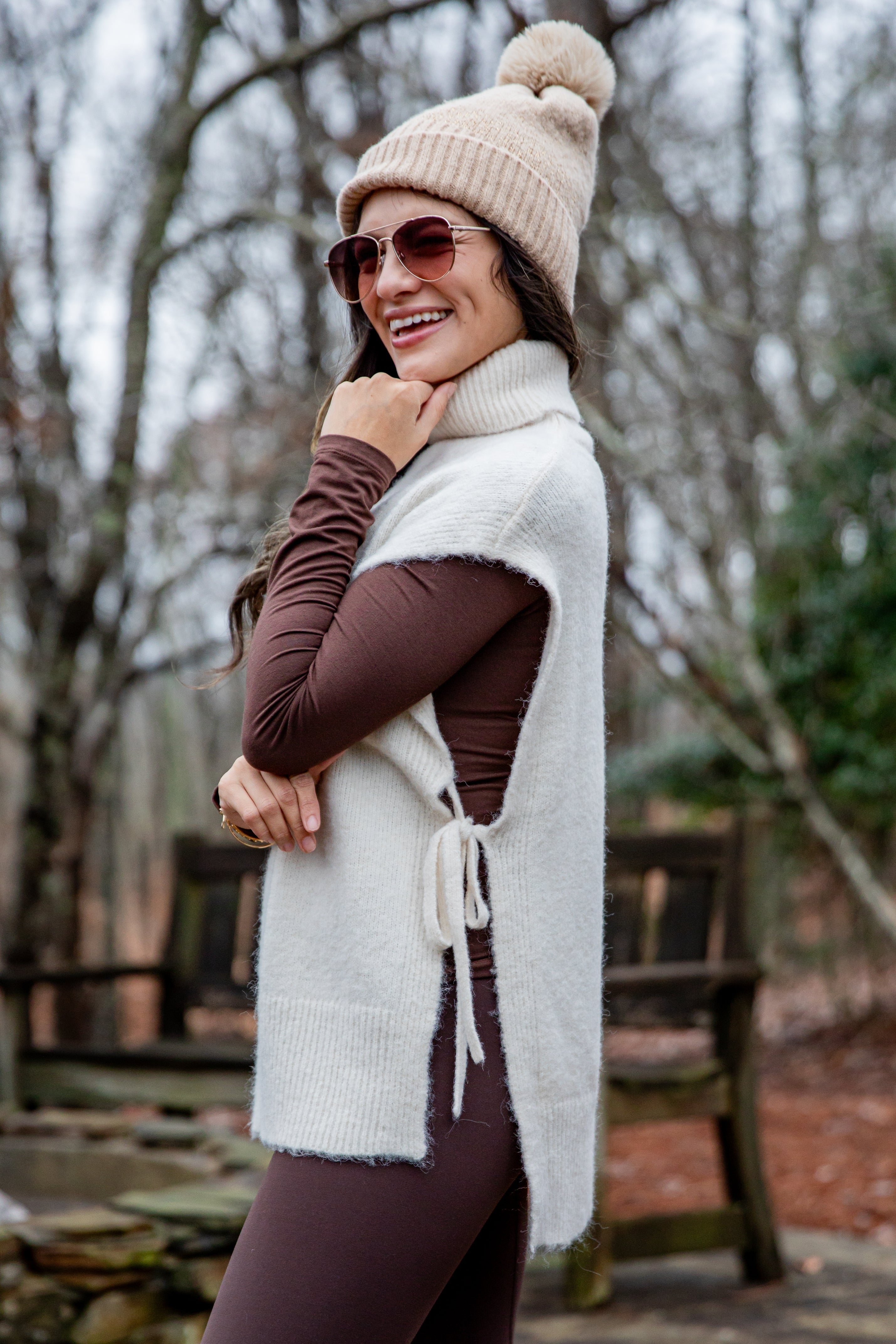 Woman wearing a white scarf, brown sweater, and beige beanie outdoors.