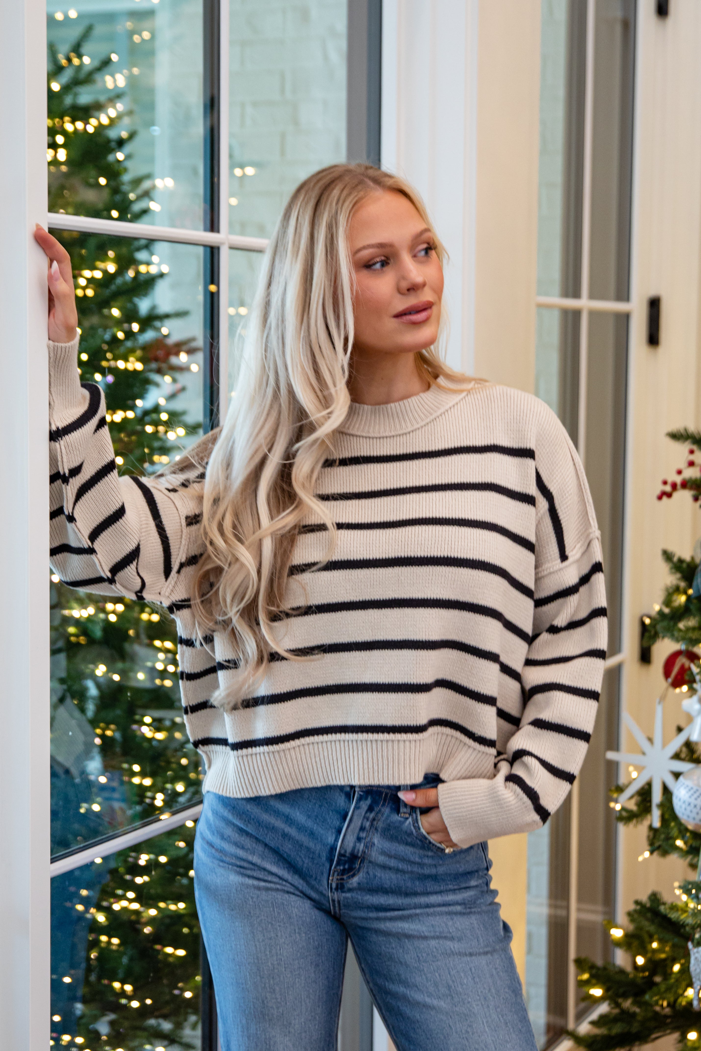 Woman wearing a striped sweater and jeans standing in front of a decorated Christmas tree.