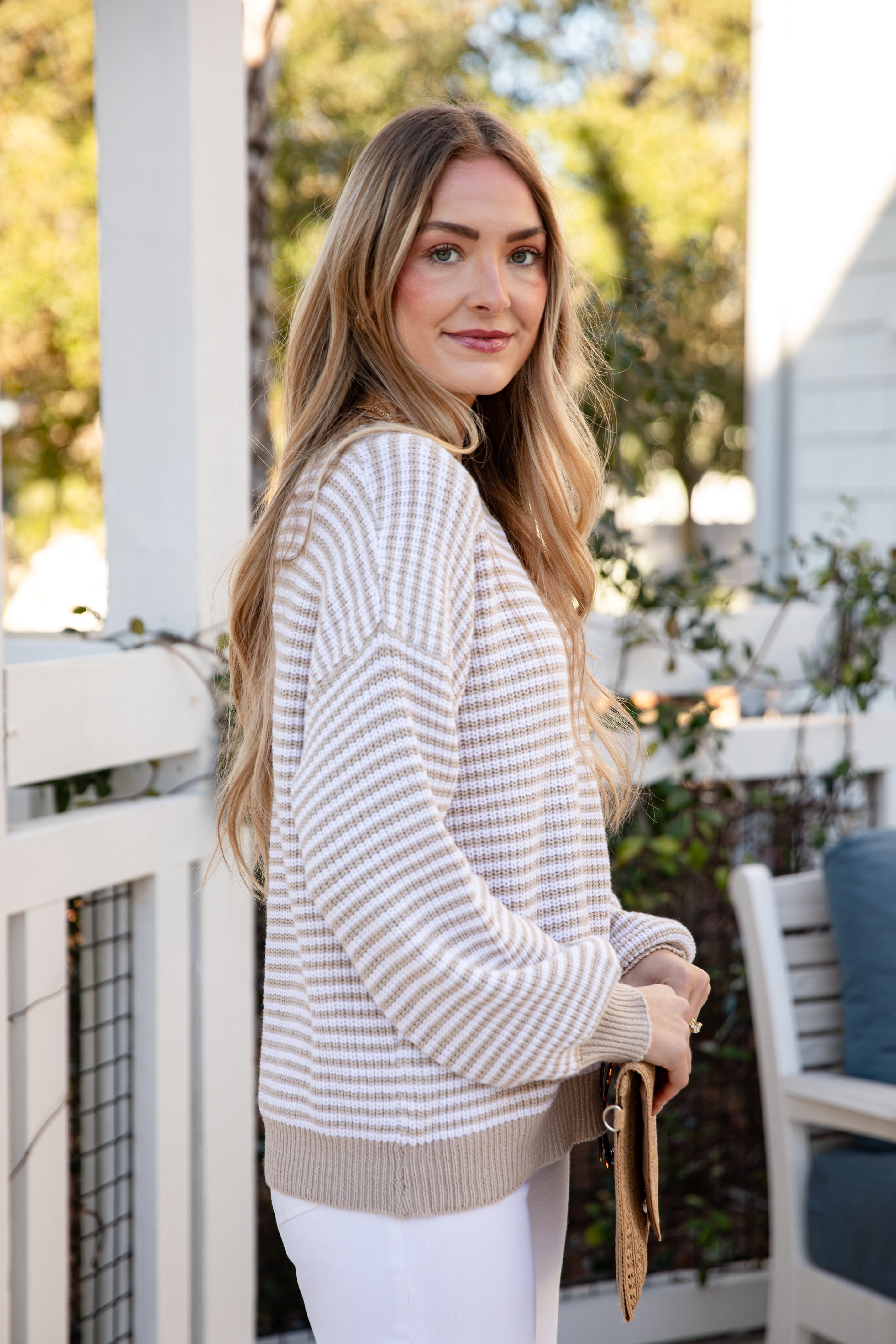 Woman wearing a striped sweater on a porch with plants and furniture in the background