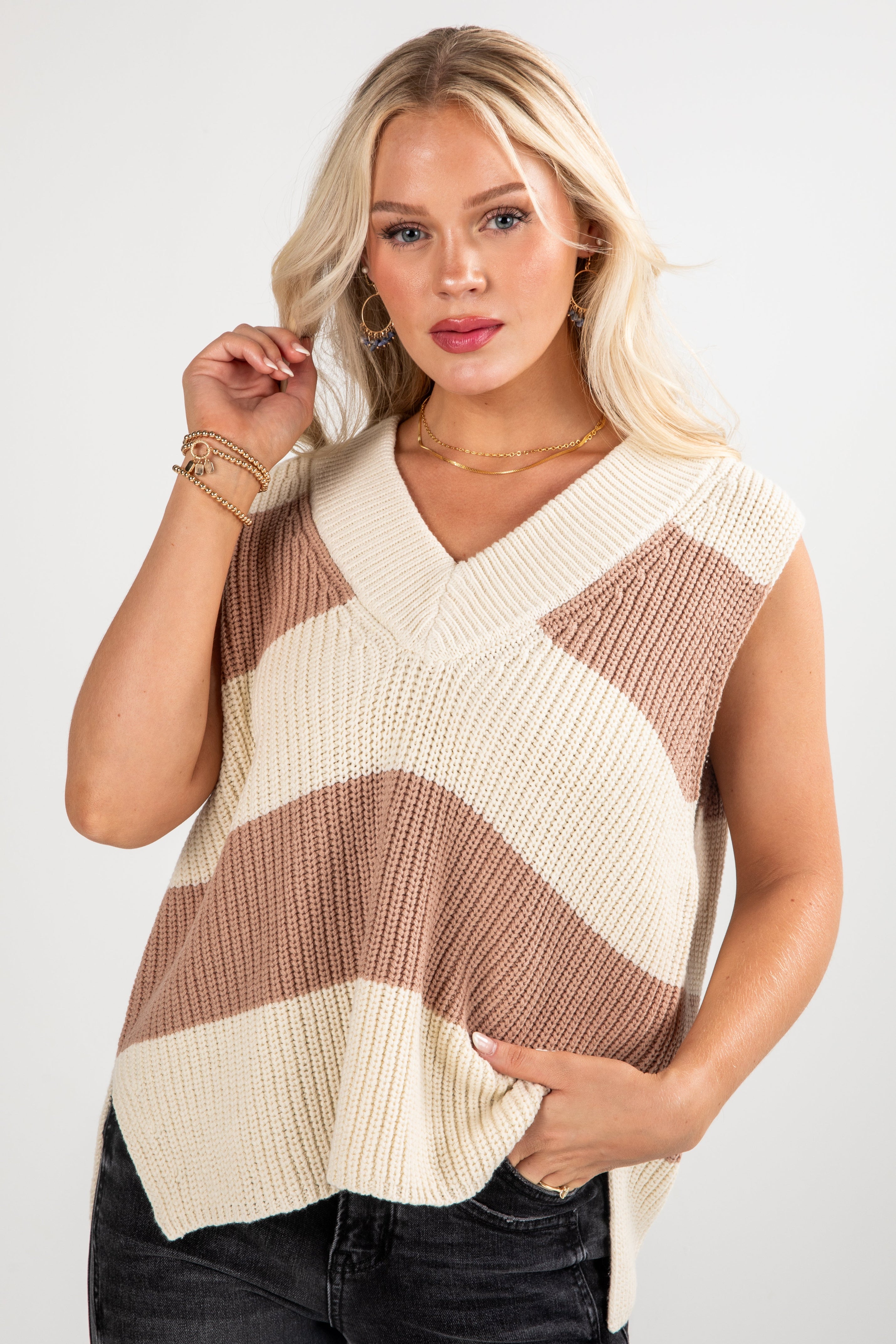 Woman wearing a beige and brown striped sleeveless sweater on a white background