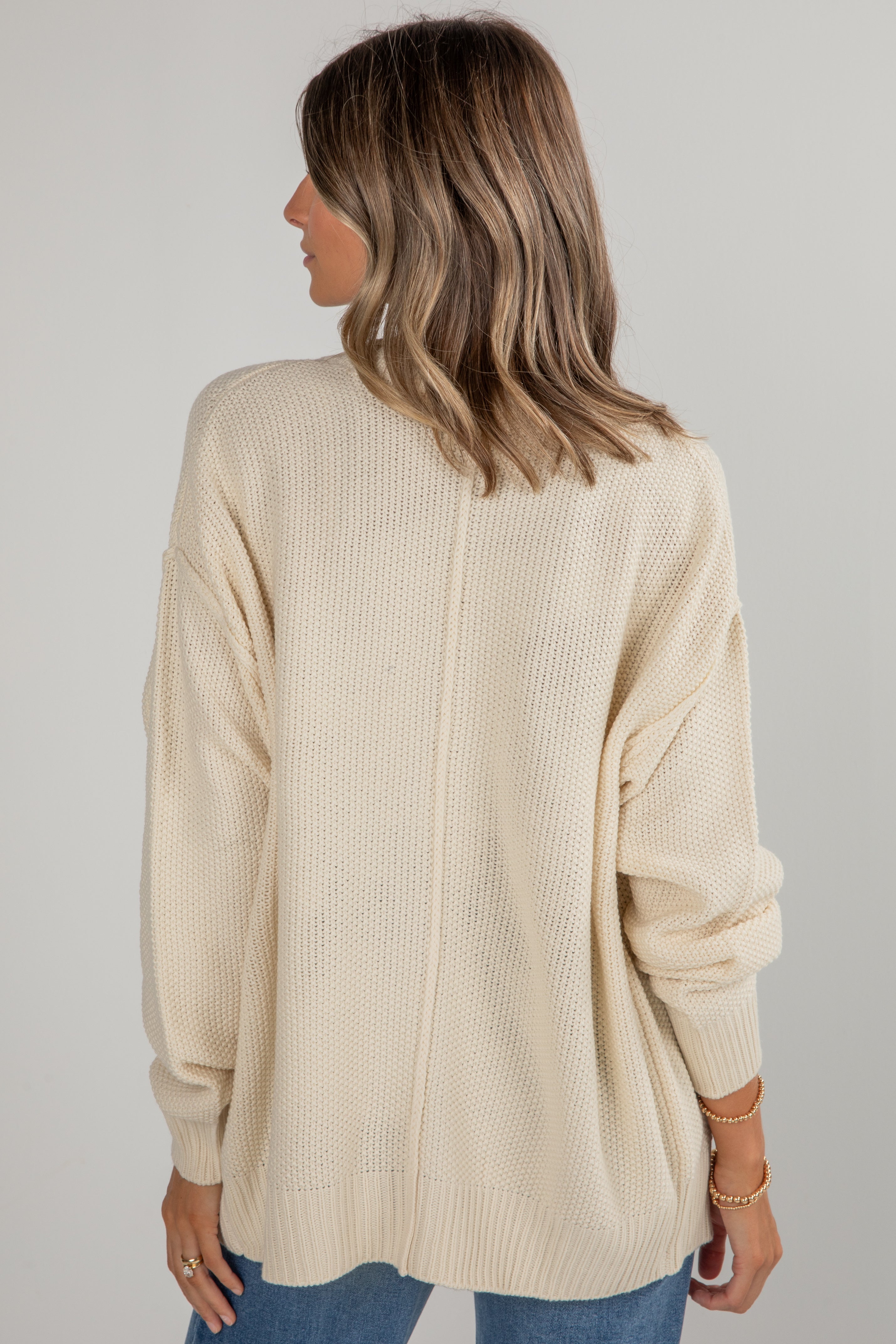 Woman wearing a beige ribbed sweater against a plain background