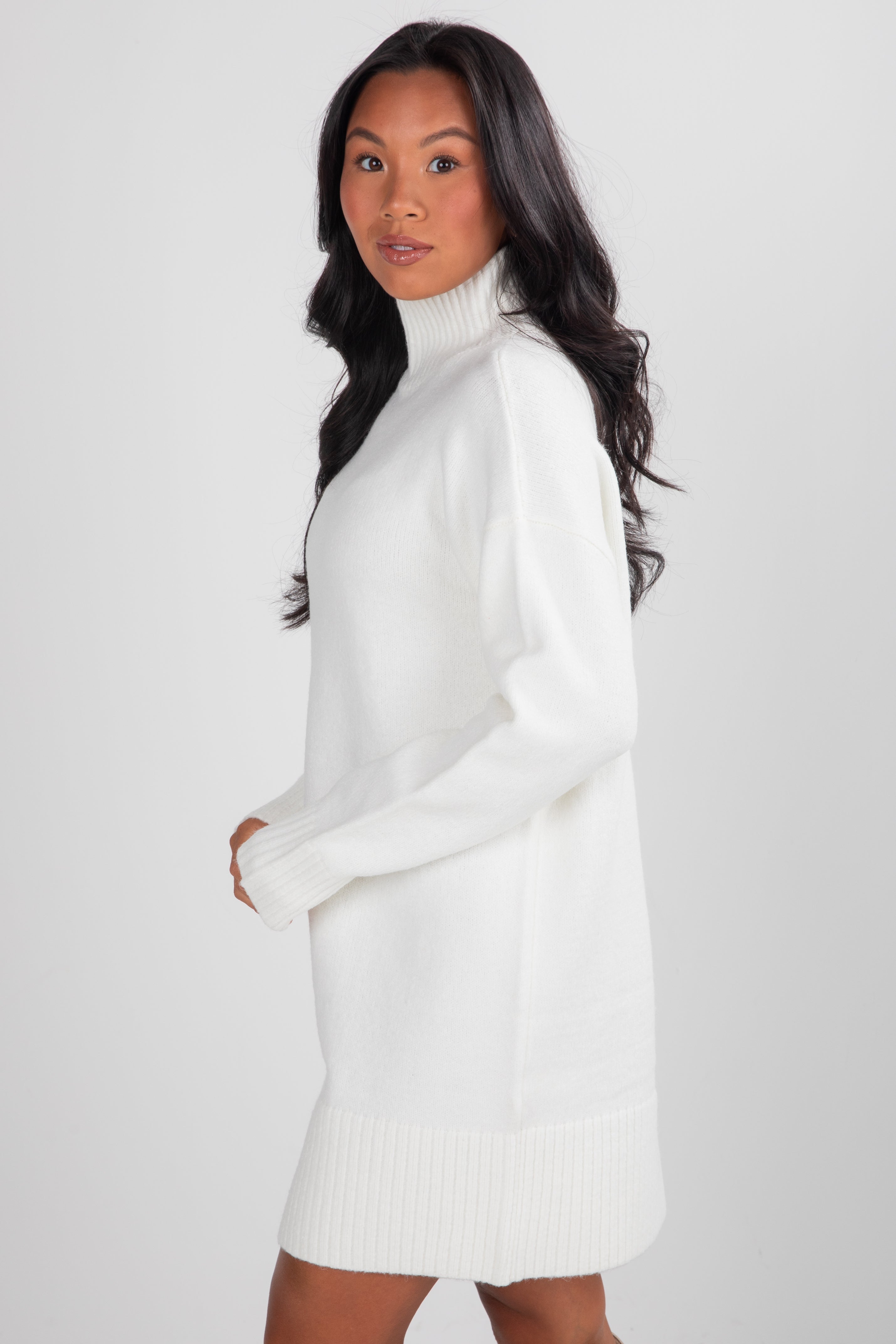 Woman wearing a white turtleneck dress against a plain background