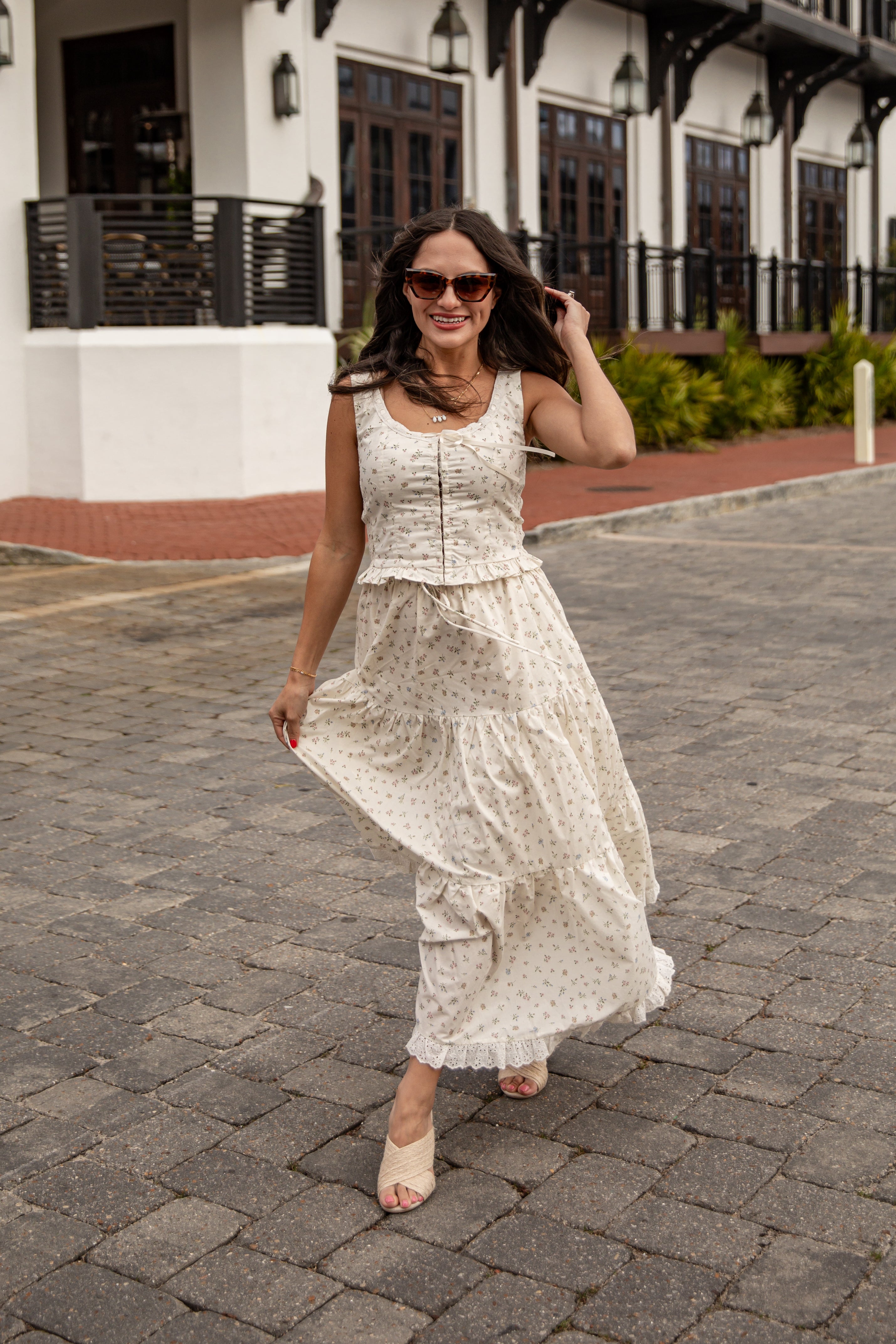Woman in a white floral dress walking on a paved street.