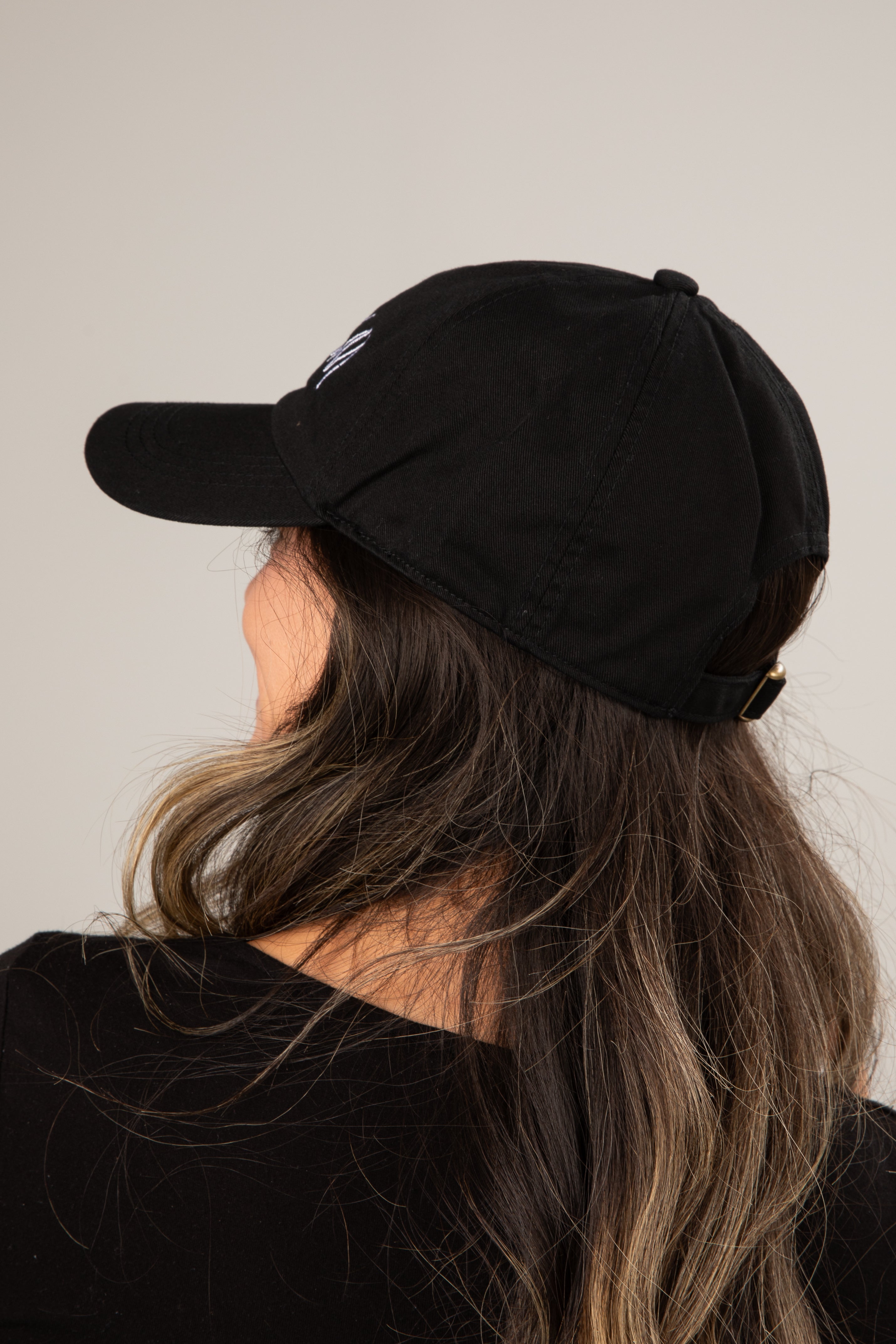 Person wearing a black cap with a logo on a plain background