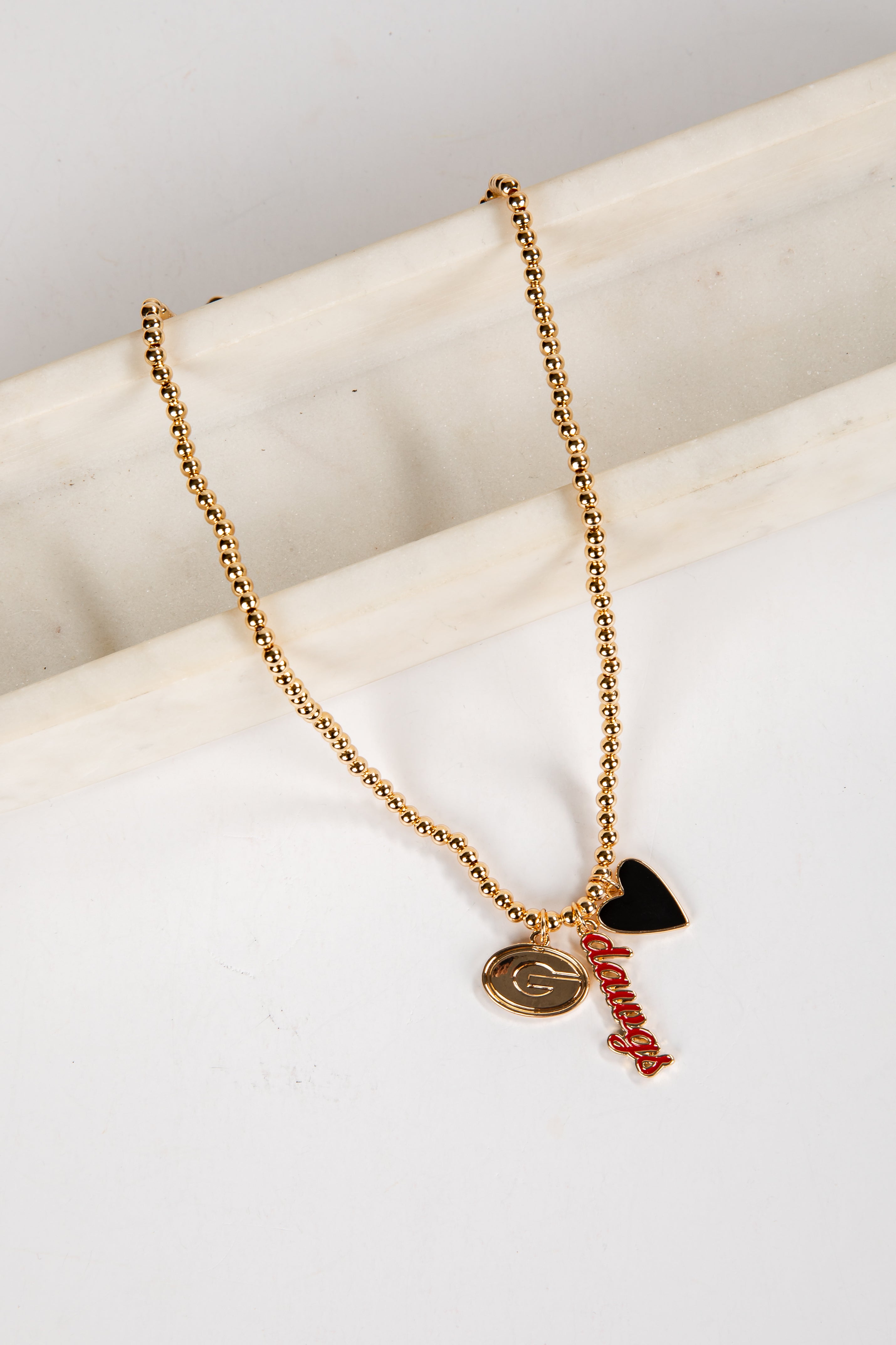 Gold necklace with heart and letter pendant on a white surface