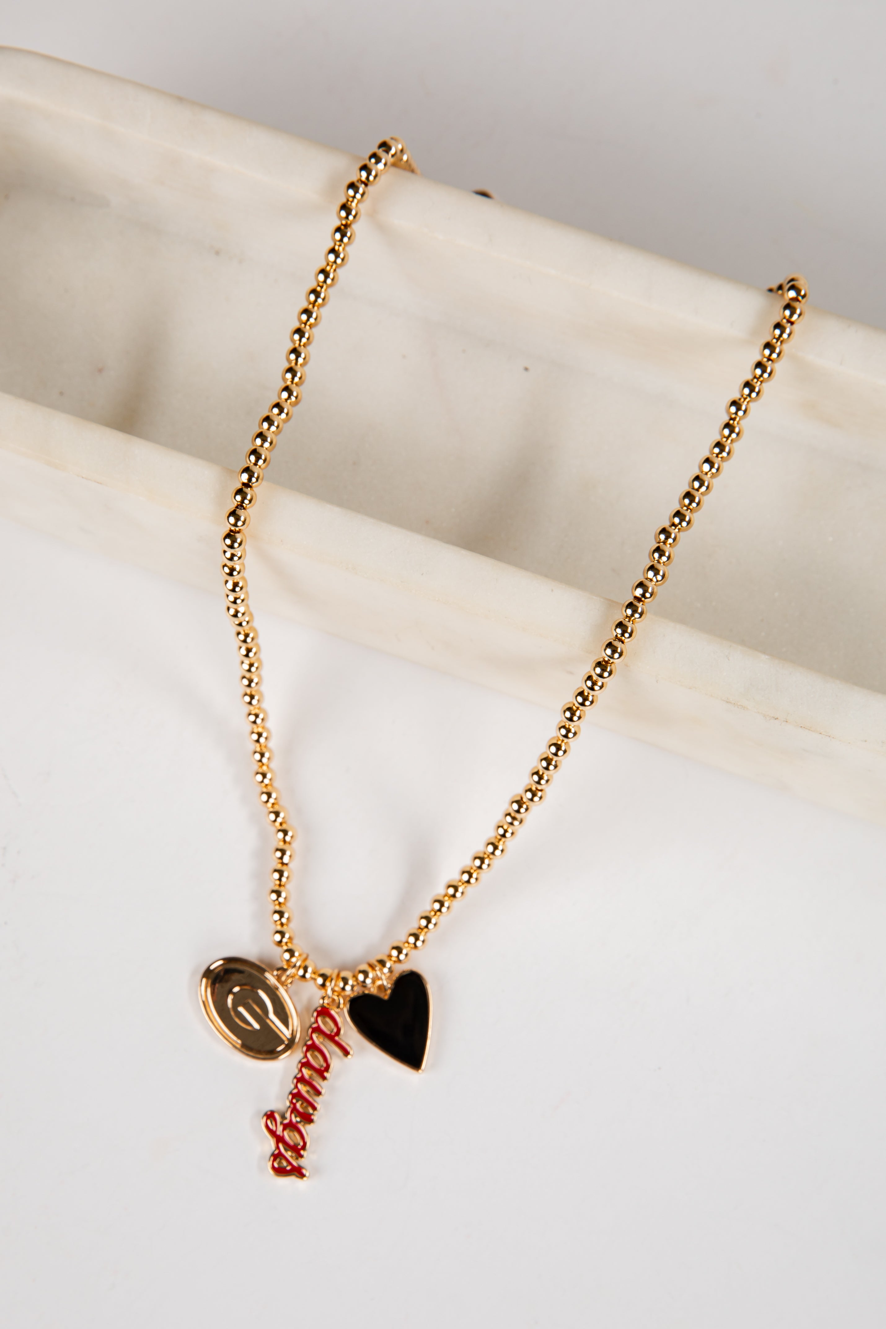 Gold necklace with heart and leaf pendants on a marble surface