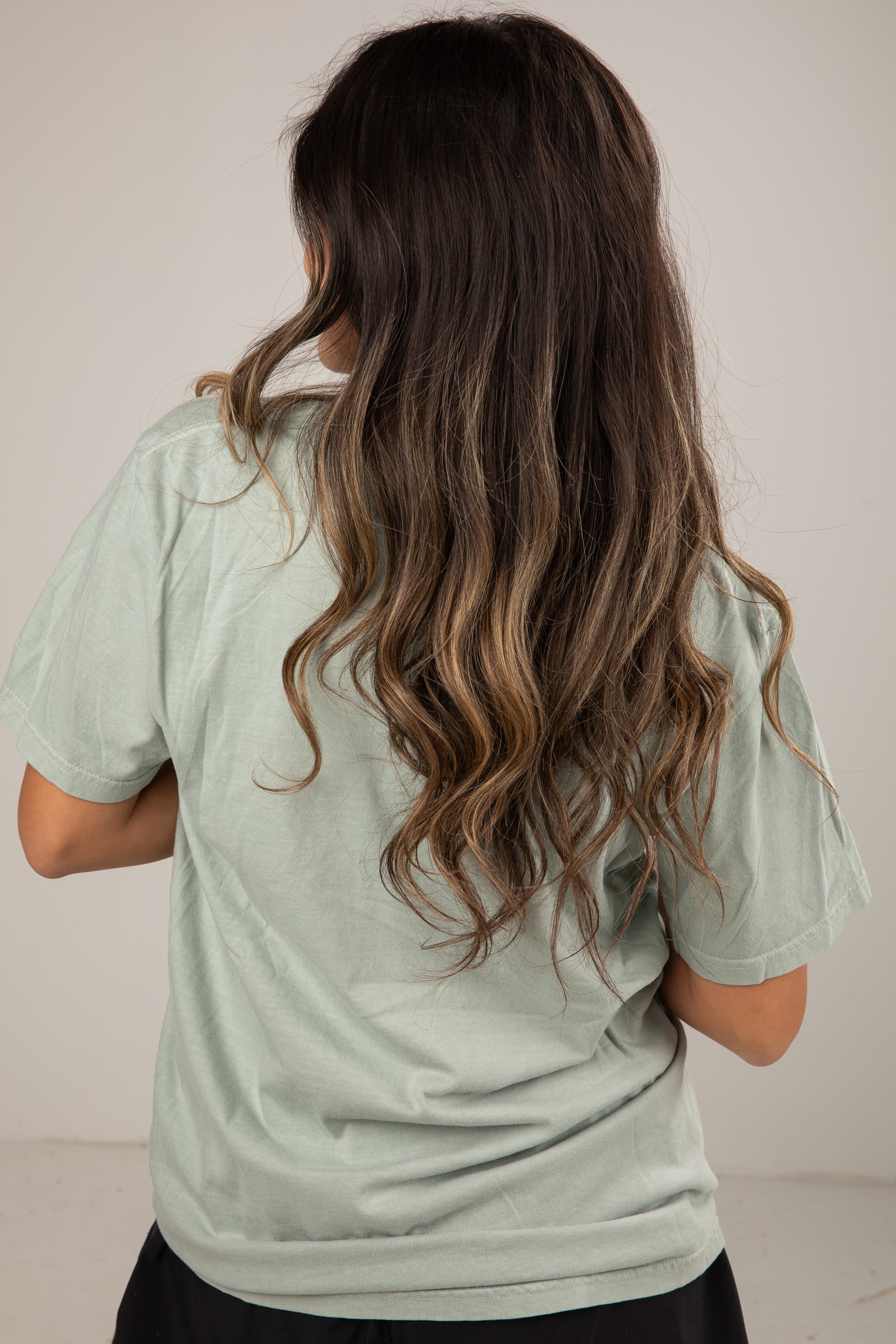 Person wearing a light green shirt with long, wavy hair on a plain background