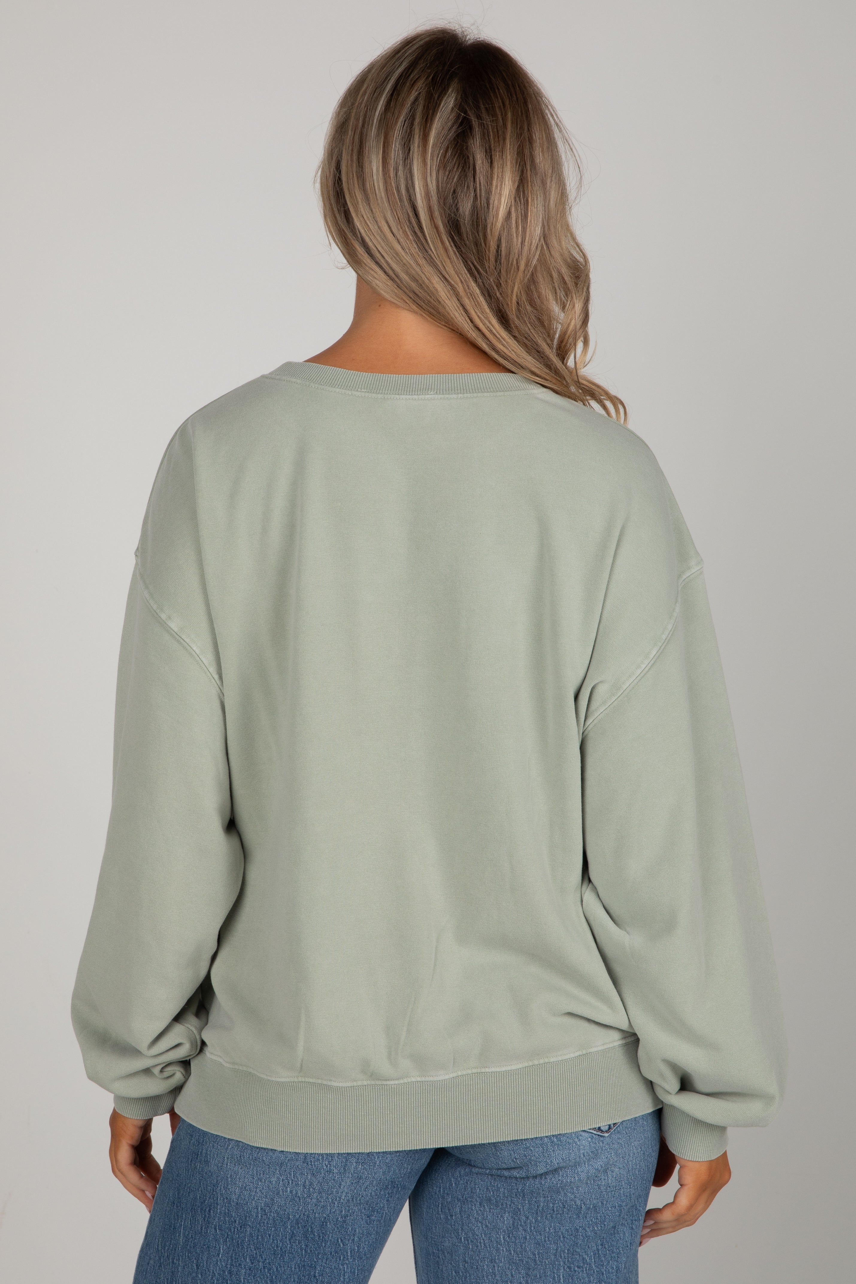 Person wearing a light green sweatshirt and blue jeans on a plain background