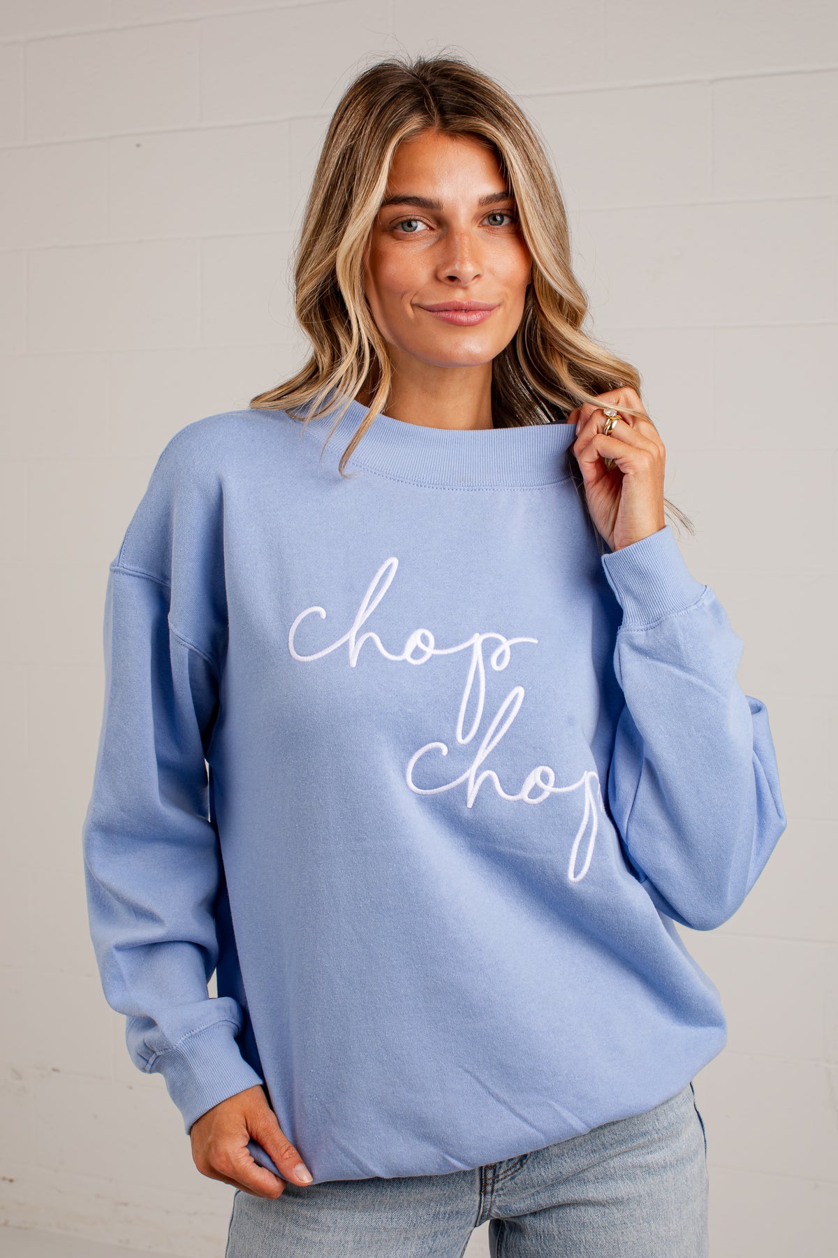 A woman wearing a light blue crewneck sweatshirt with &