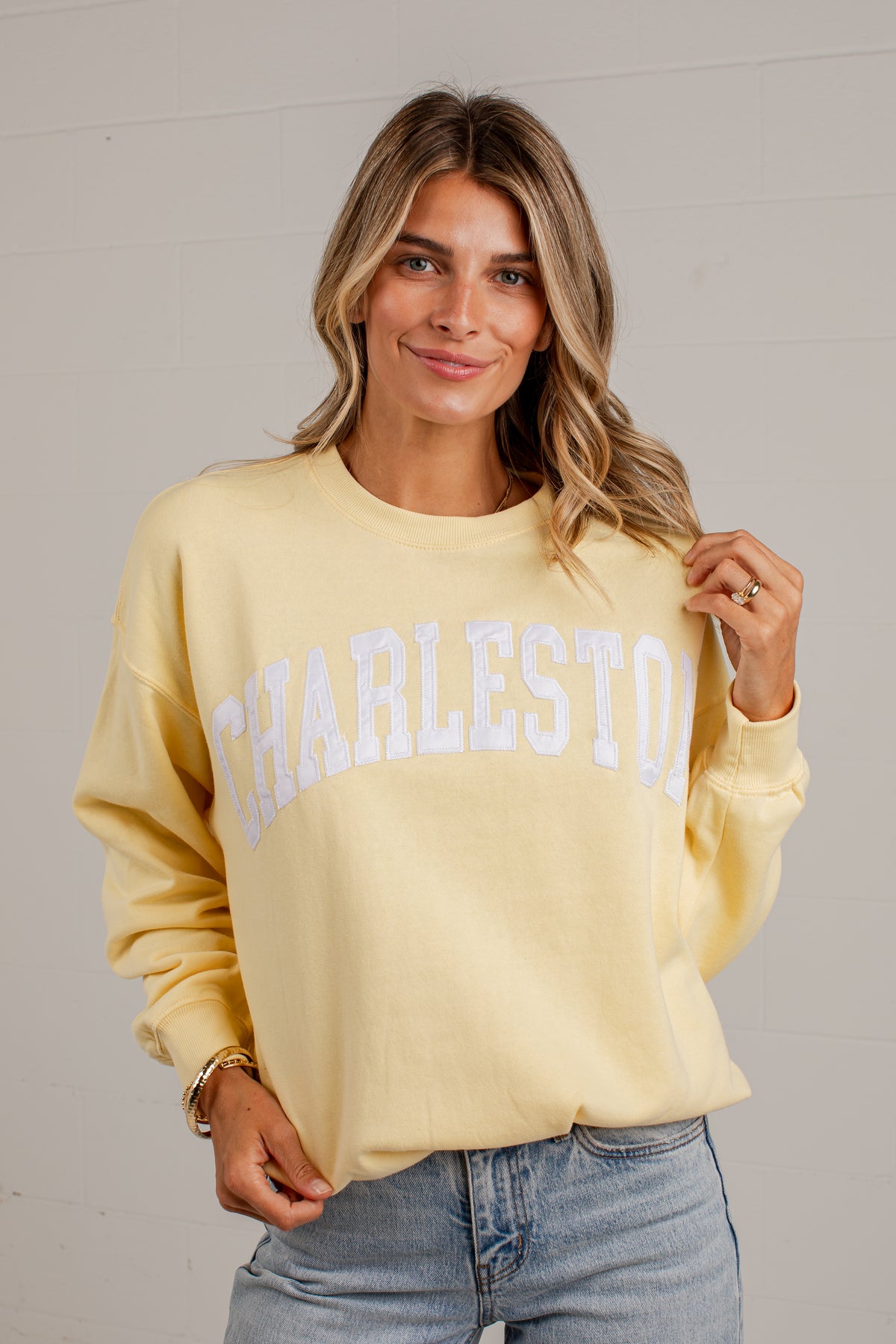 A woman wearing a pale yellow crewneck sweatshirt with &