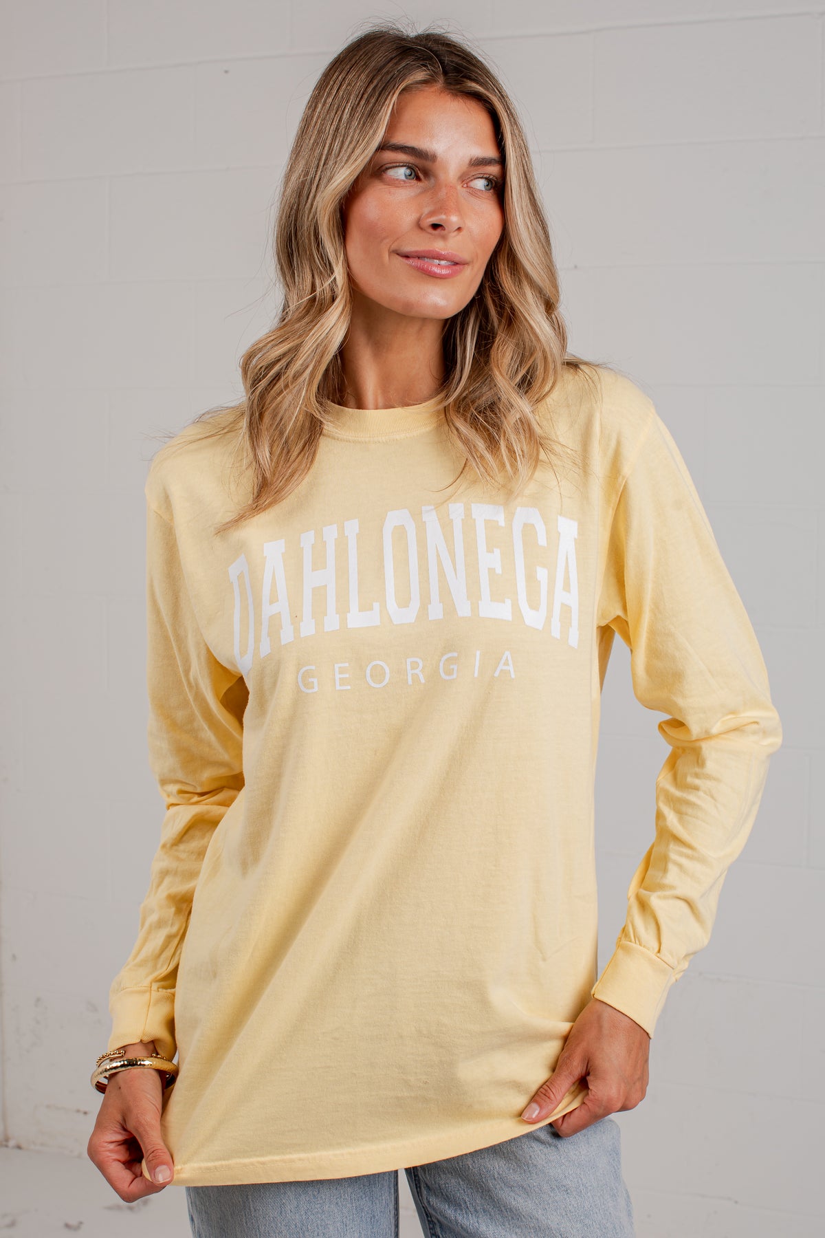 A woman wearing a pale yellow long-sleeve t-shirt with &