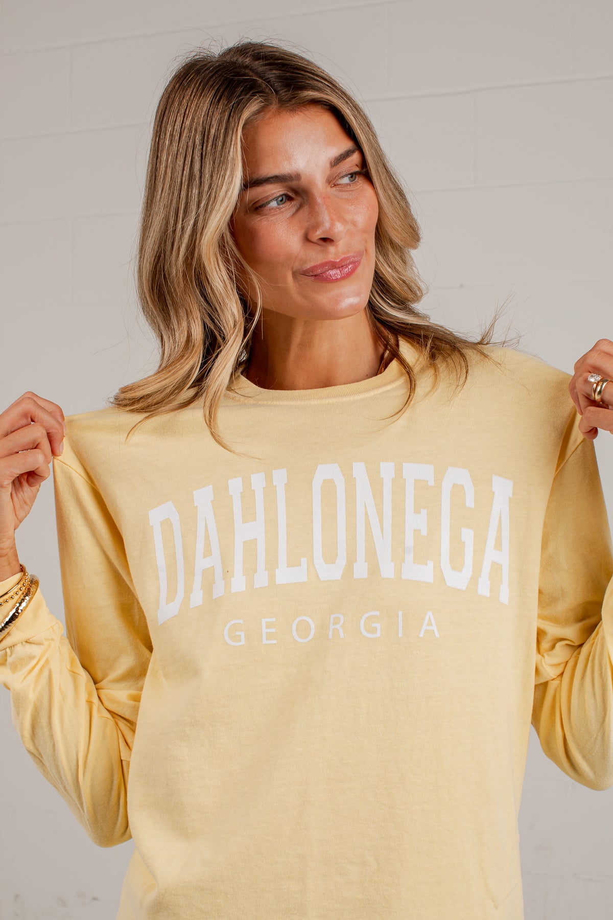 A woman wearing a pale yellow long-sleeve sweatshirt with &