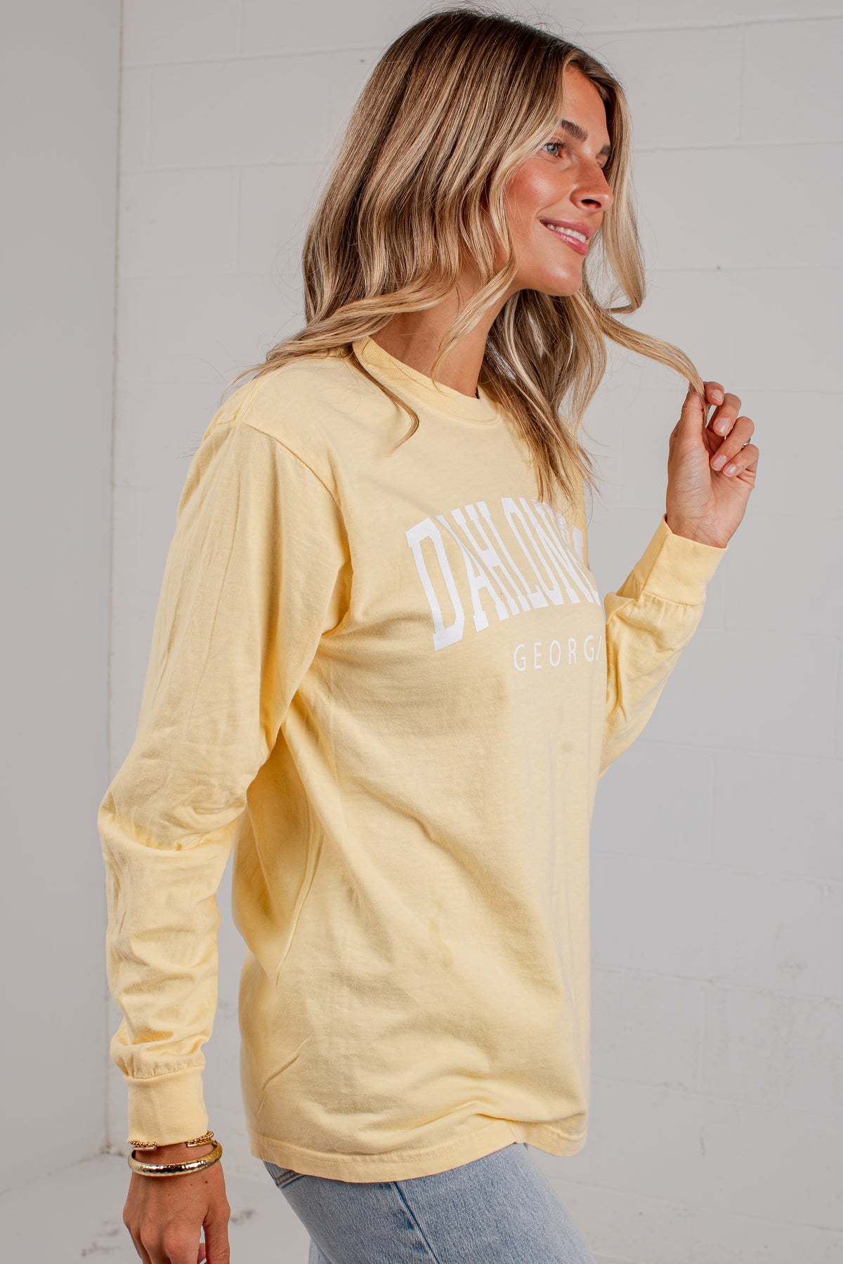 A woman wearing a pale yellow long-sleeve t-shirt with &