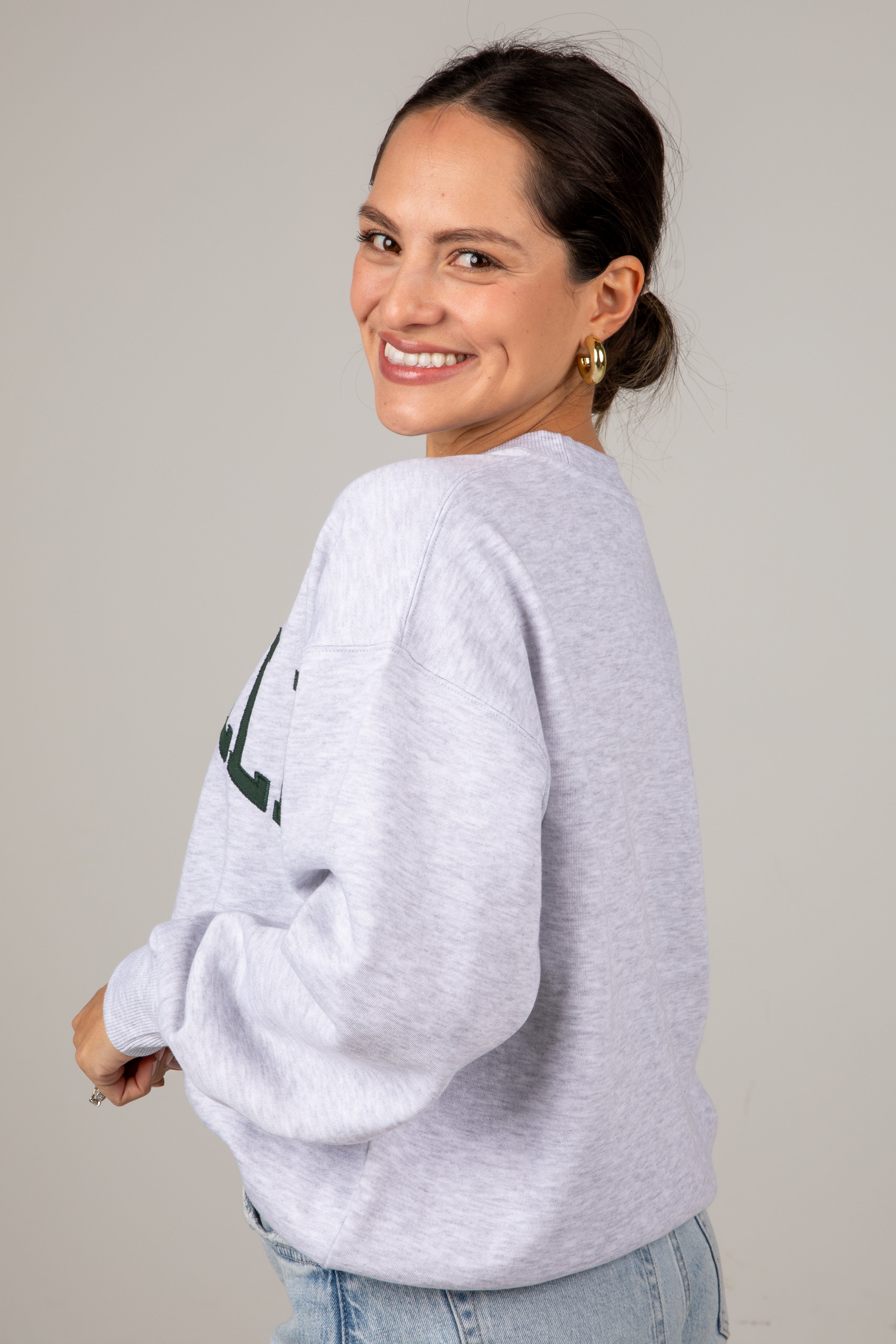 Woman wearing a light gray sweatshirt with text on the back, standing against a plain background