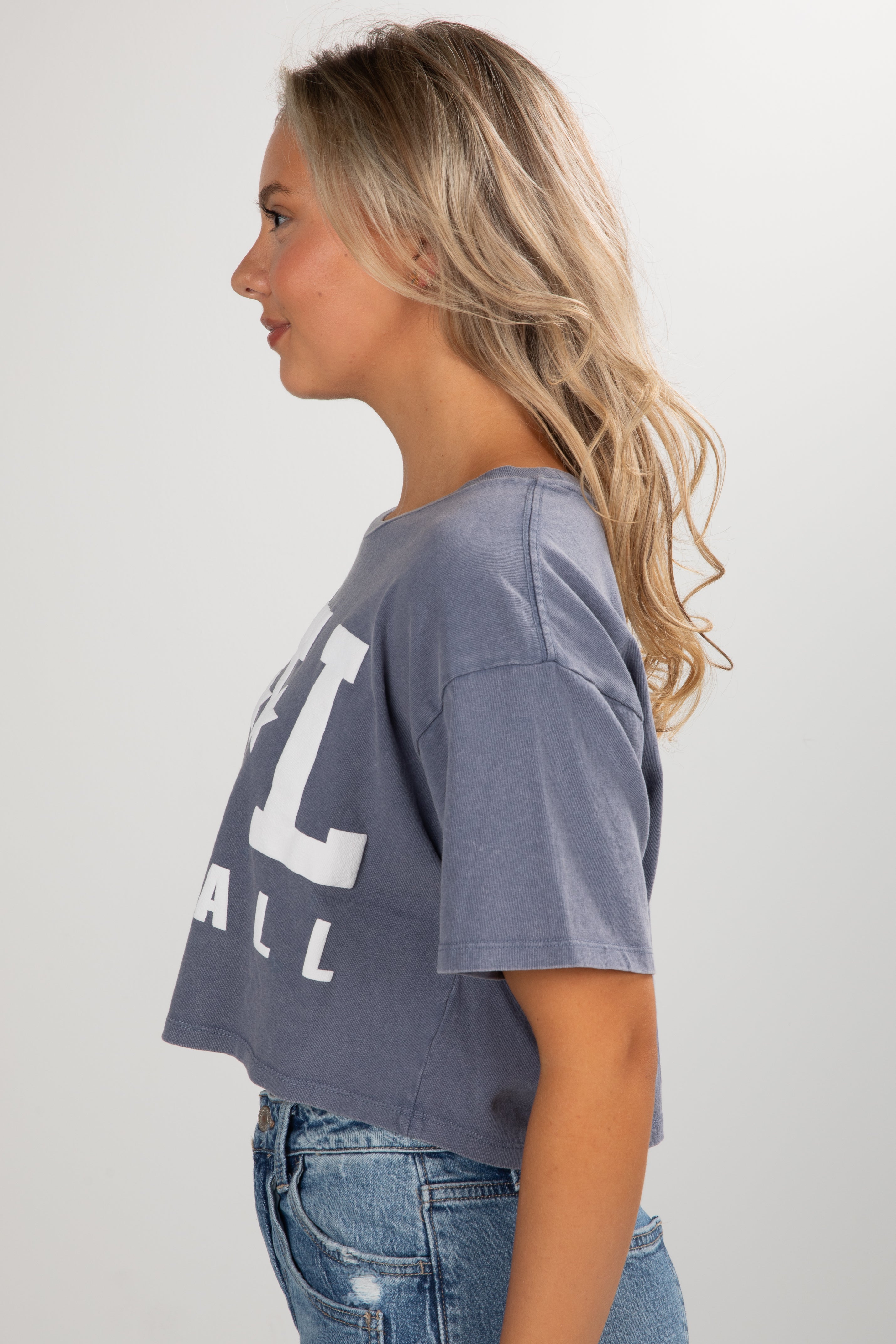Woman wearing a gray t-shirt with text and blue jeans on a plain background