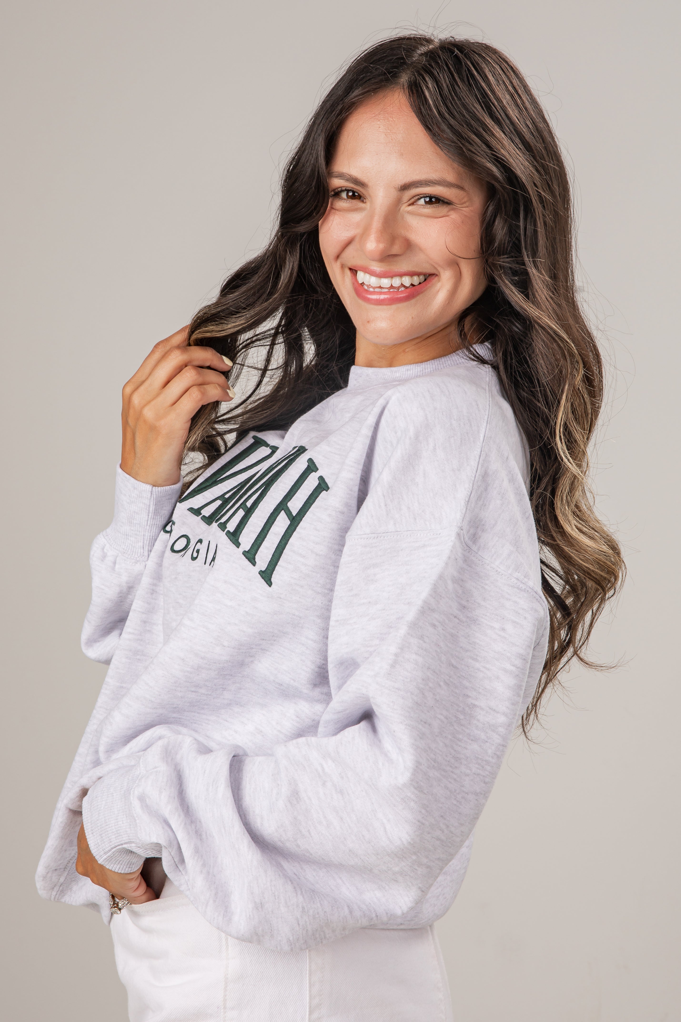 Woman wearing a light gray sweatshirt with text, smiling against a plain background