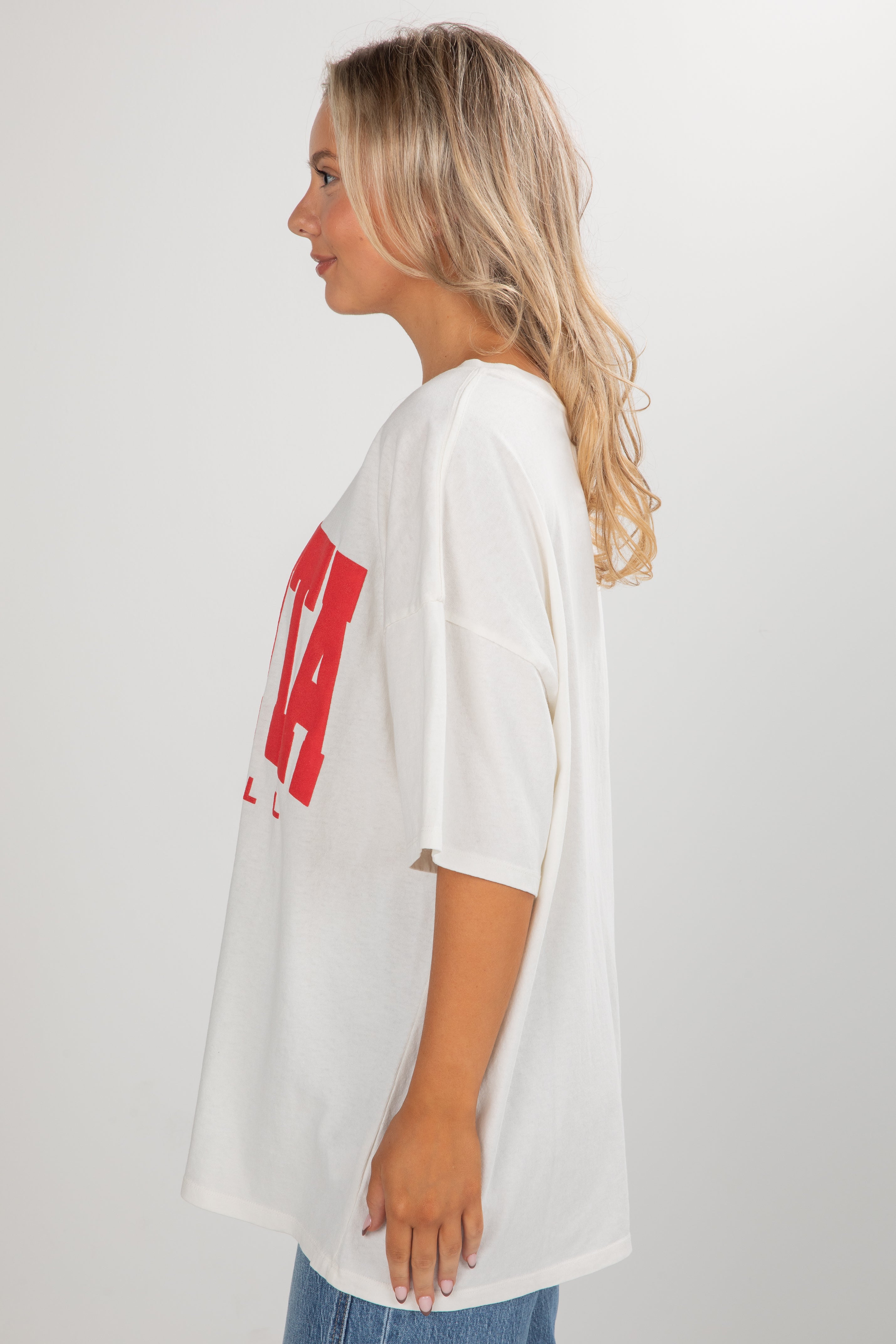Woman wearing a white oversized t-shirt with red text on a plain background