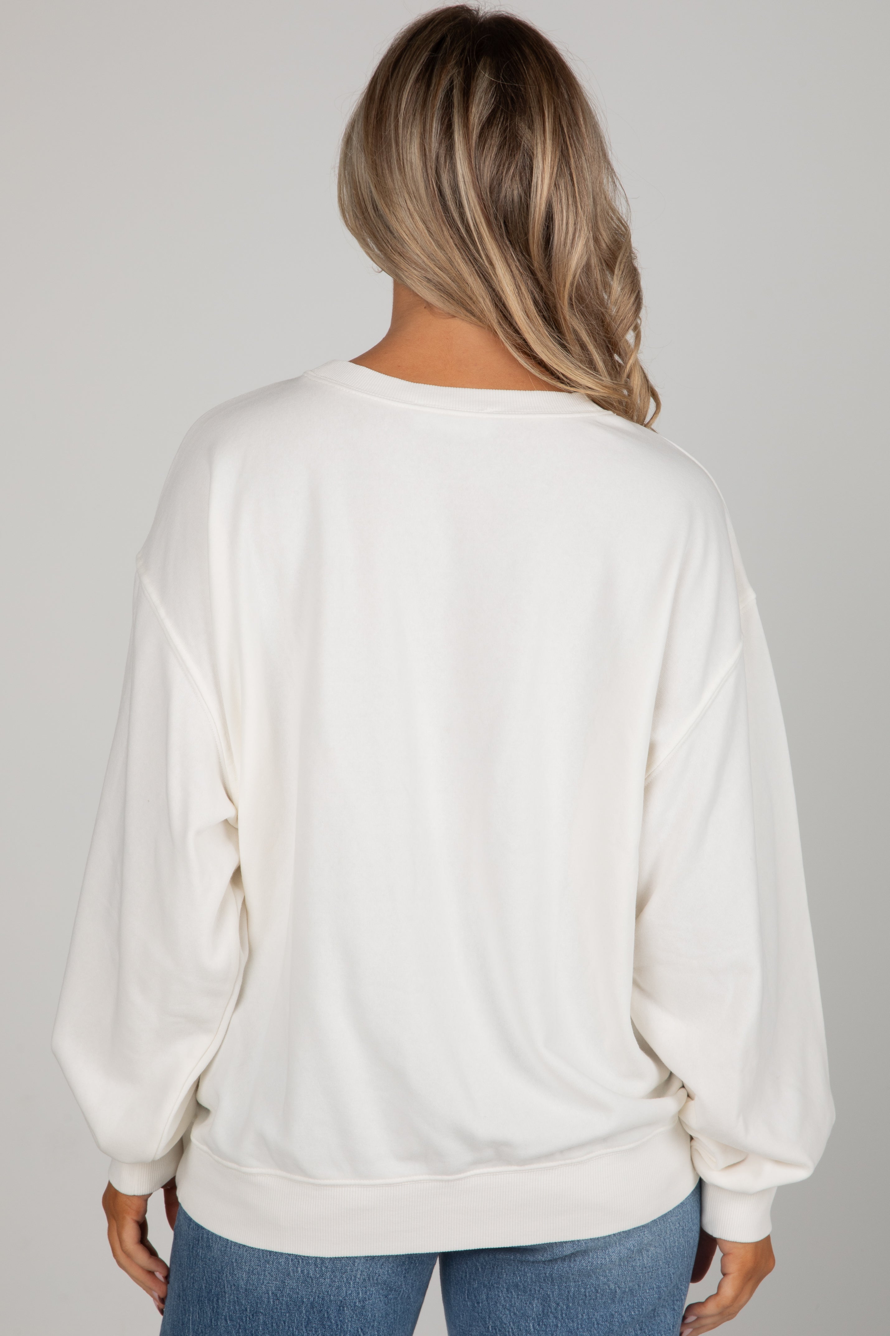 Person wearing a white sweatshirt and blue jeans on a plain background