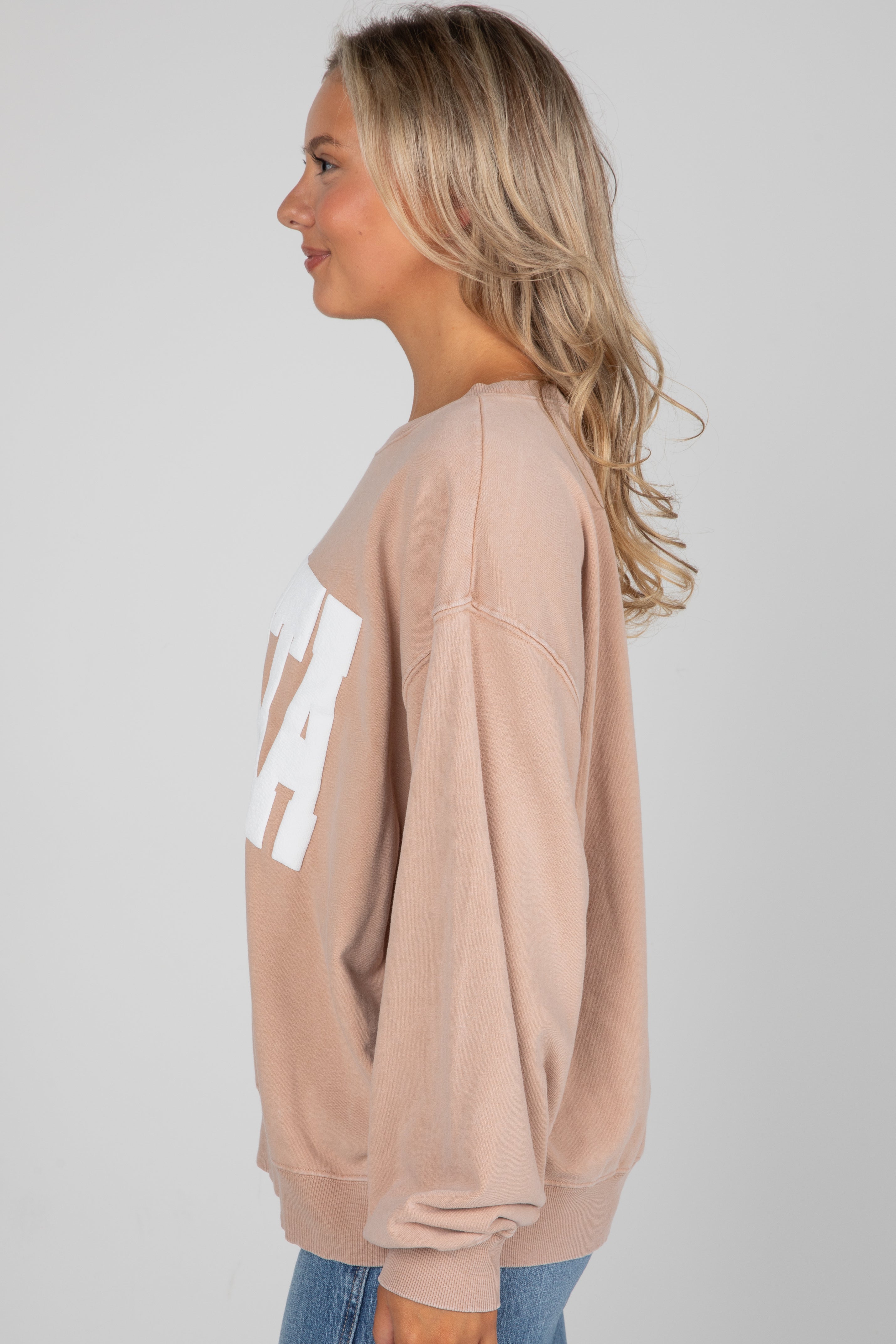 Woman wearing a beige sweatshirt with a logo on a plain background