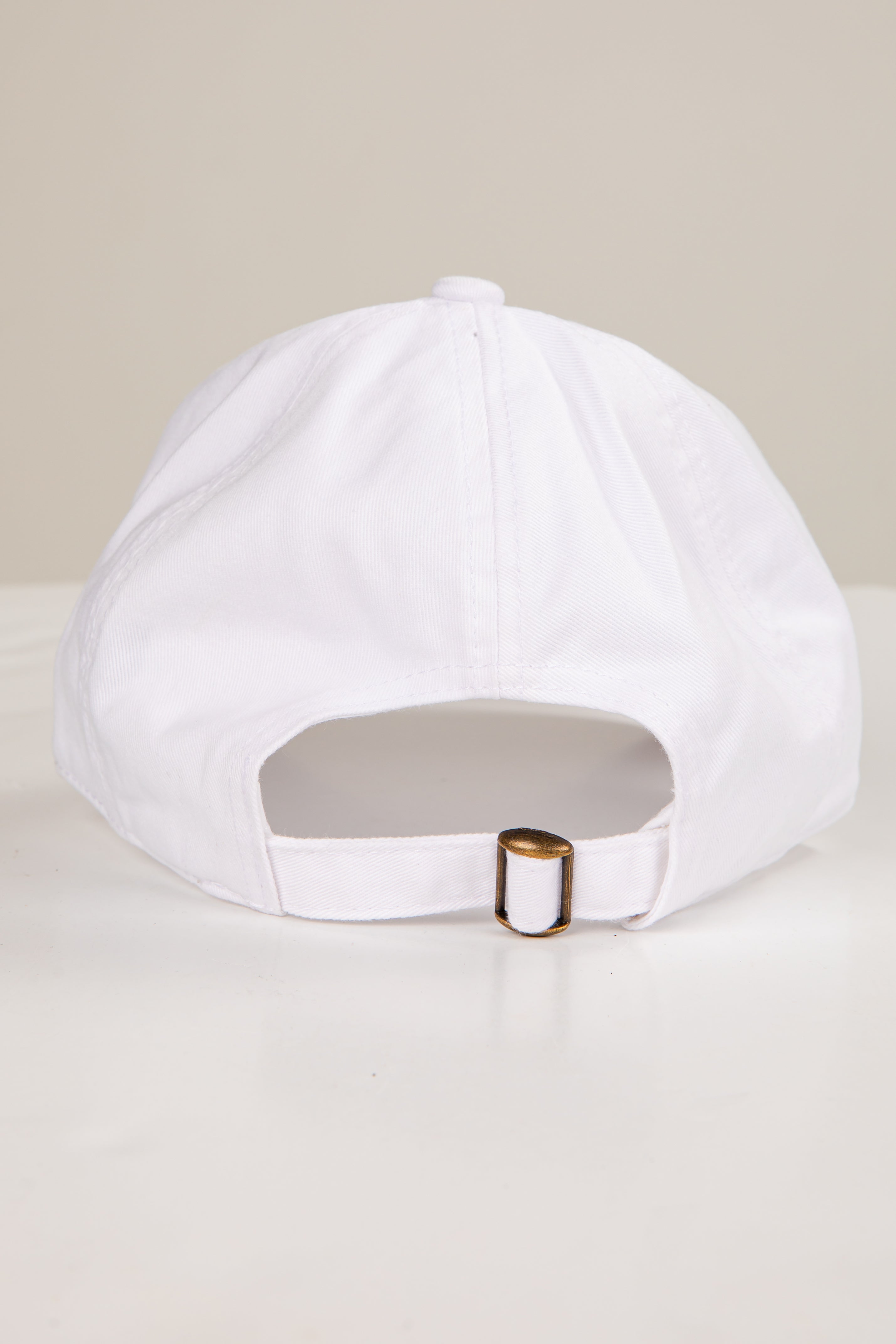 White cap with a gold buckle on a light beige background