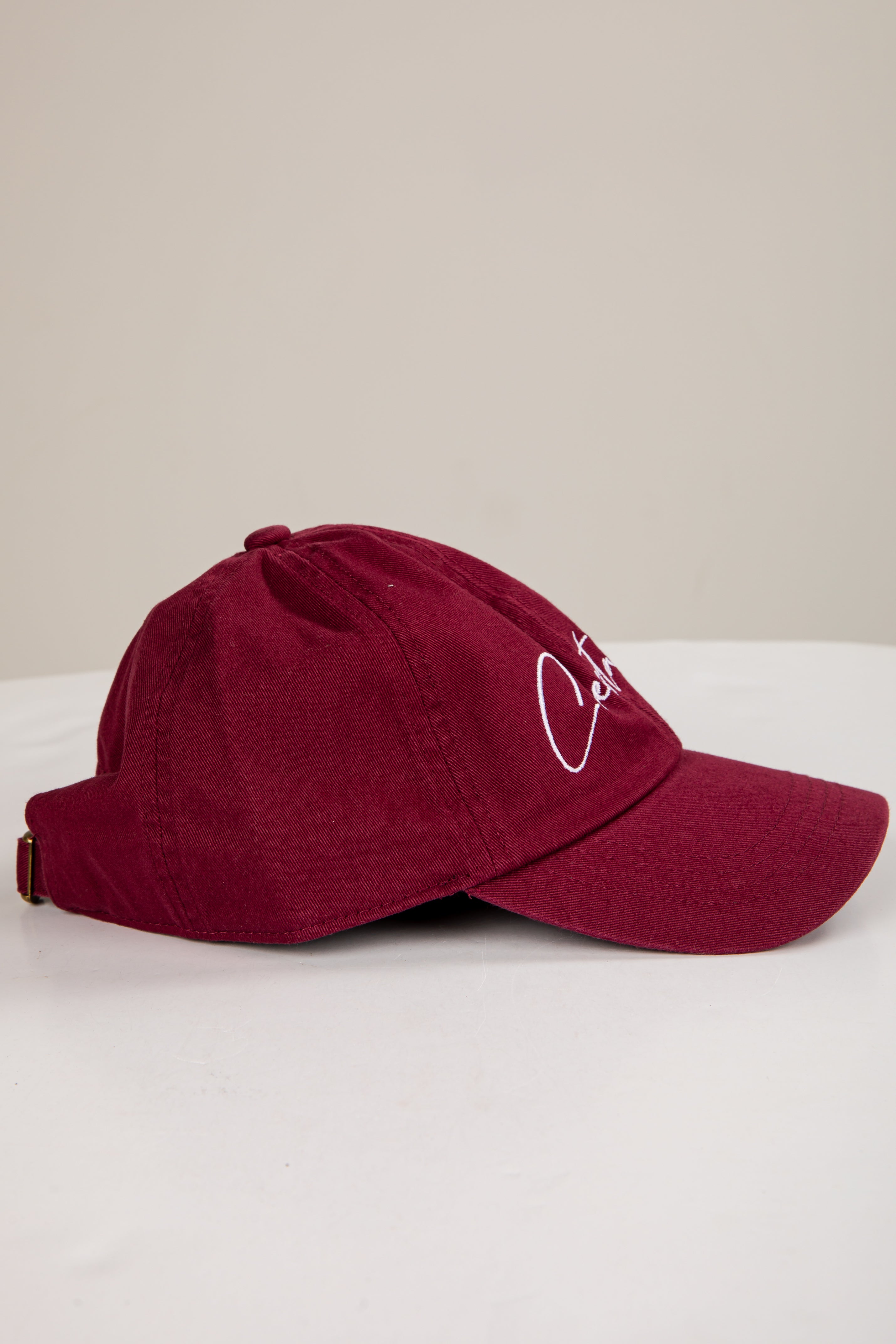 Maroon baseball cap with a logo on a white surface