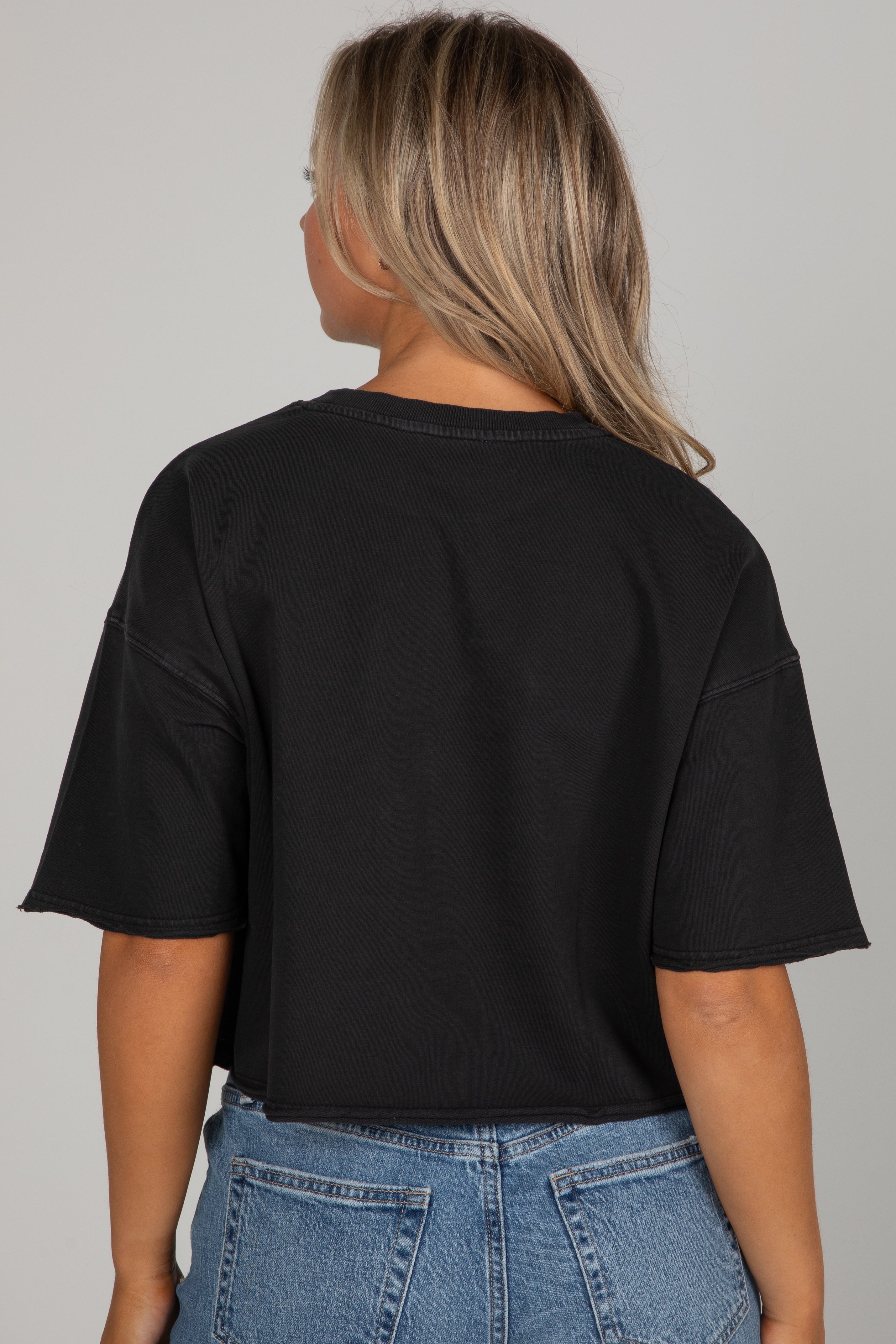 Person wearing a black t-shirt and blue jeans on a plain background